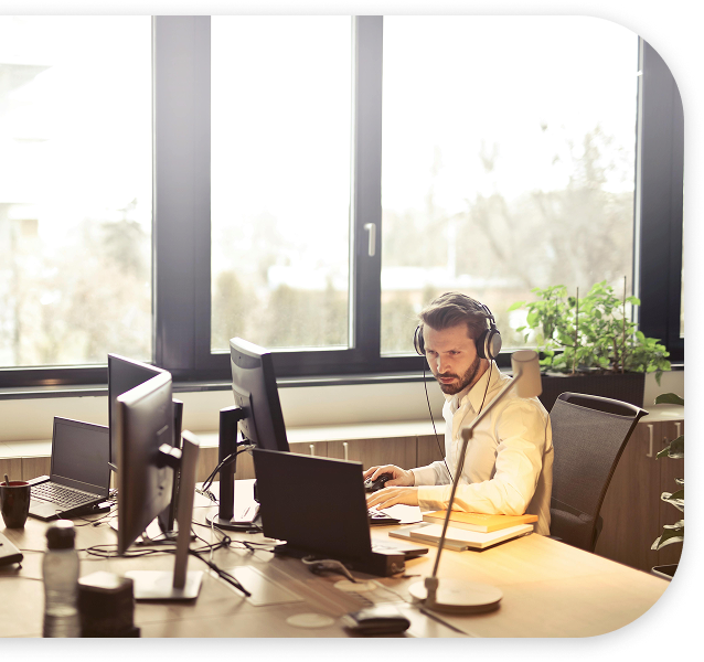 Hombre trabajando en oficina con múltiples monitores y auriculares.