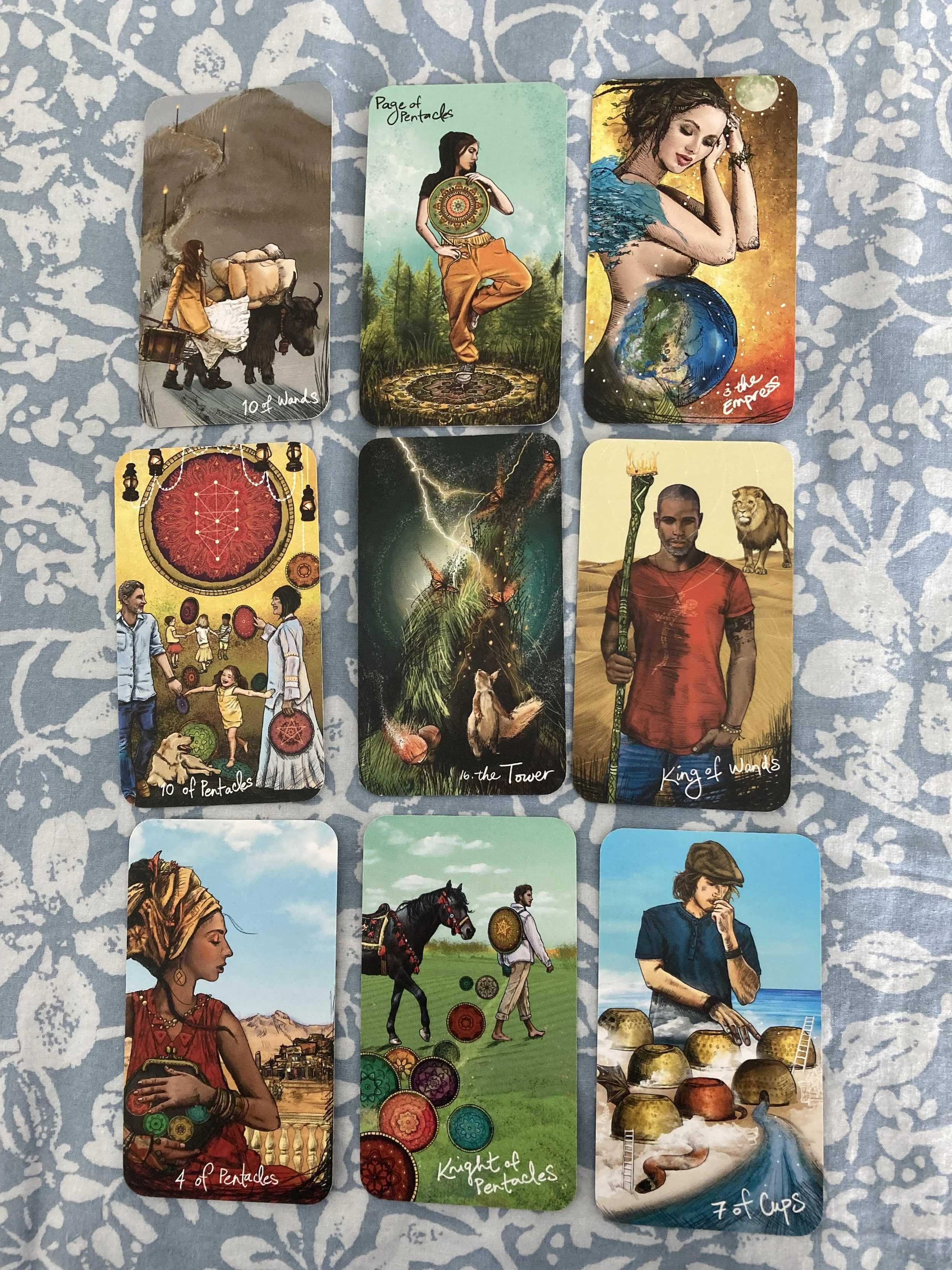 A spread of tarot cards on a blue and white patterned cloth. Light Seer's Tarot deck. 9 card spread.