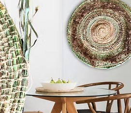 Decorative wall plate hanging above a wooden dining table with chairs, next to a large woven basket or similar item.