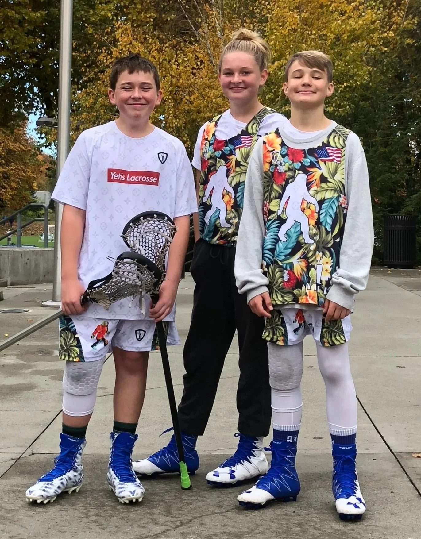 Three youth lacrosse players with their coach in tropical-print uniforms.