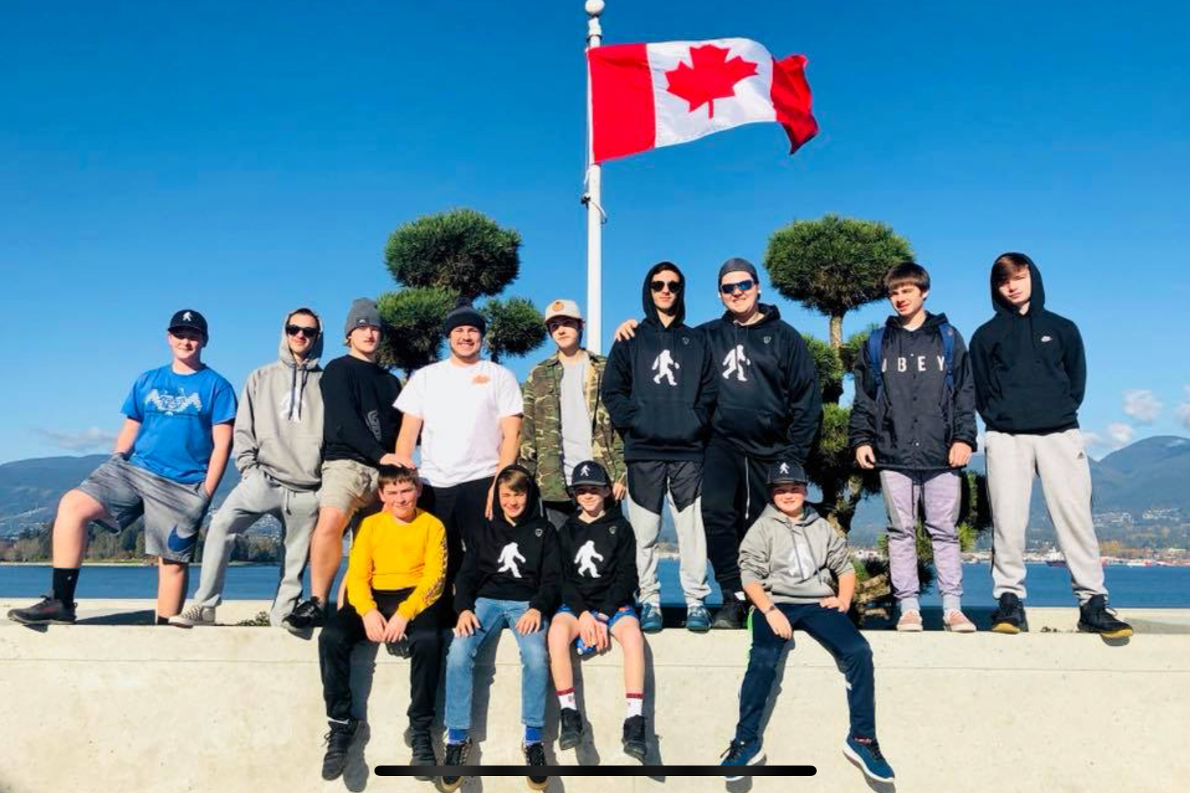 Yetis youth lacrosse players posing with a Canadian flag, water, and mountains behind them.