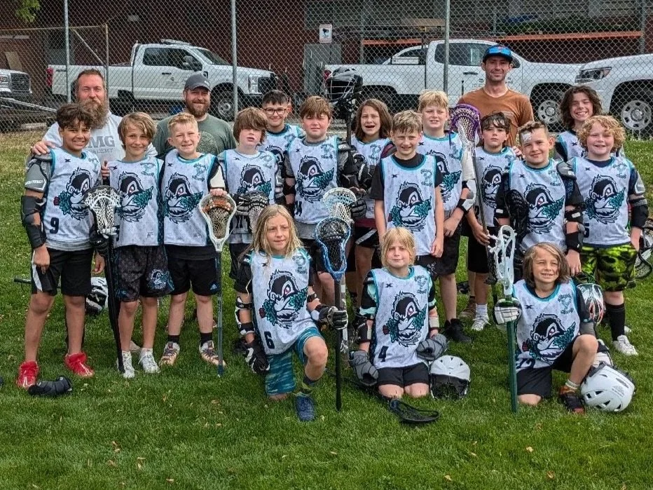 Yetis youth lacrosse team and coaches posing with sticks on a grass field.