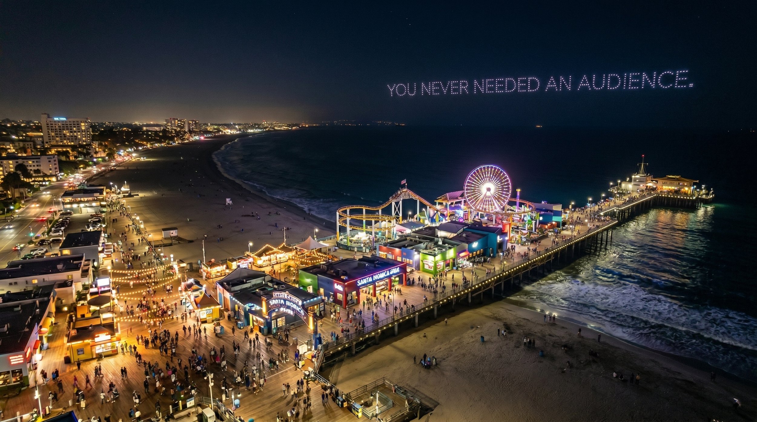 Night view of Santa Monica Pier with bright carnival rides, concession stands, and crowds of visitors, with the ocean waves crashing along the shoreline and city lights in the background. Water in the sky forms the text 'You never needed an audience.'