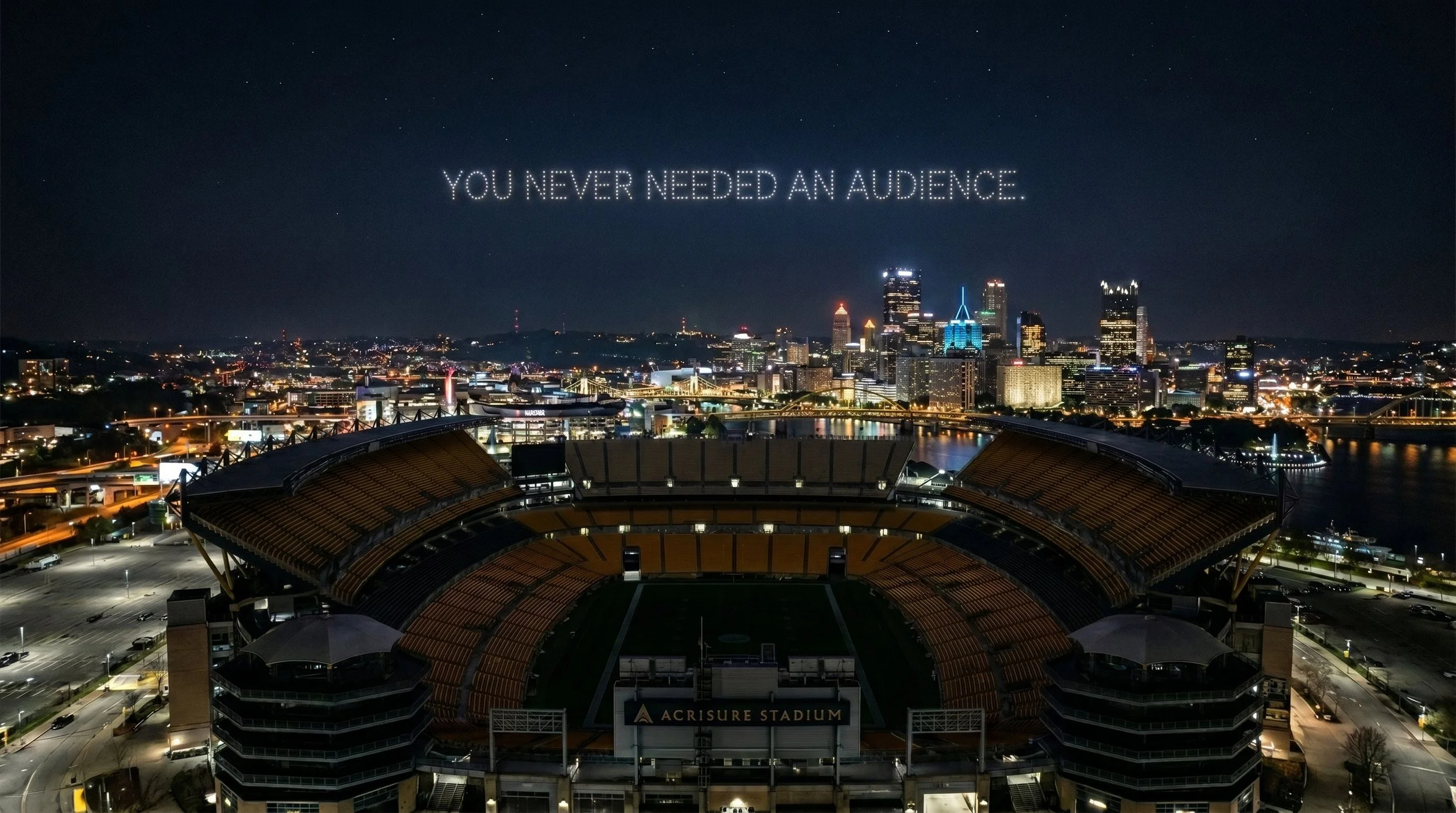 Night view of a city skyline with illuminated buildings, a stadium in the foreground named Acrisure Stadium, and a message in the sky saying "You never needed an audience".