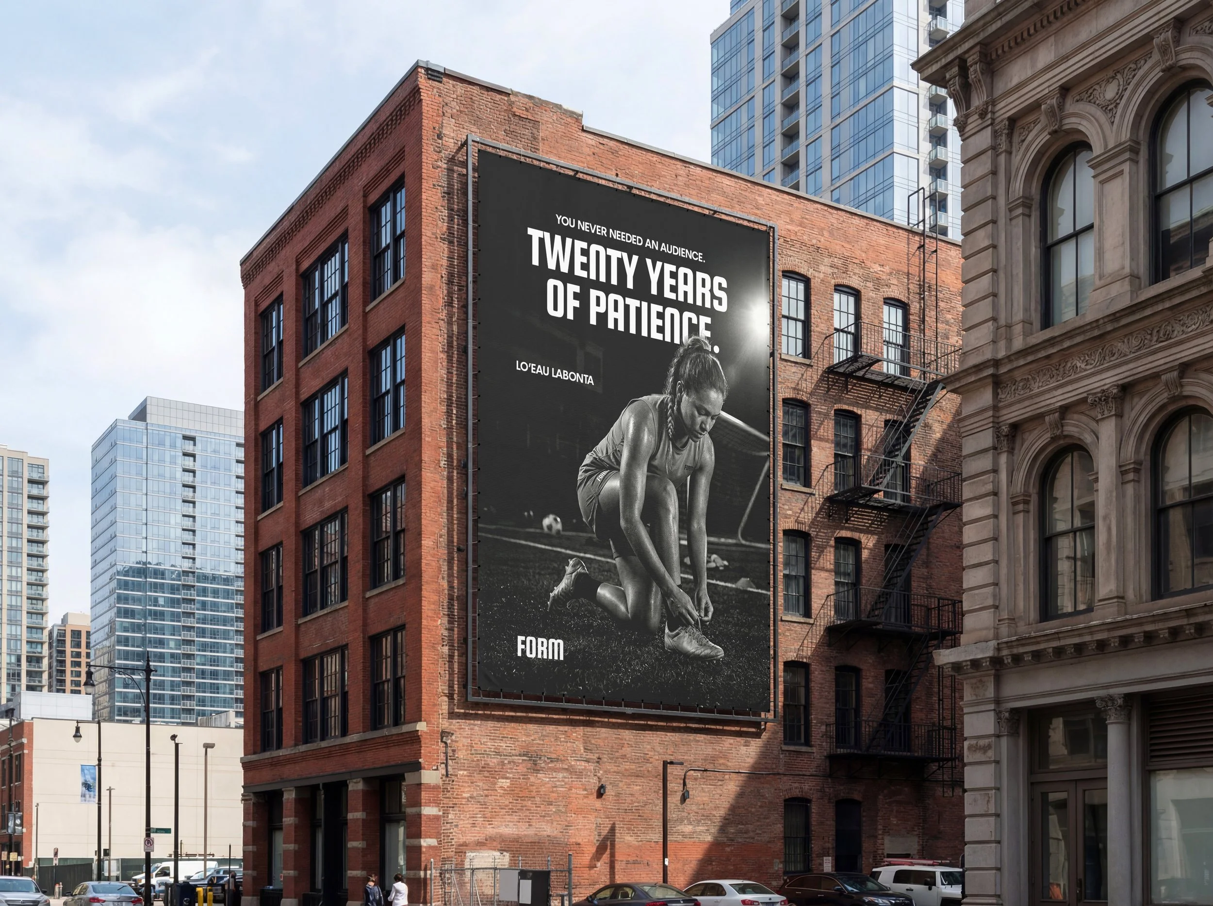 Billboard on a red brick building with the text 'You never needed an audience. Twenty years of patience.' and a black and white image of a female athlete crouching on a track with a soccer ball in the background.