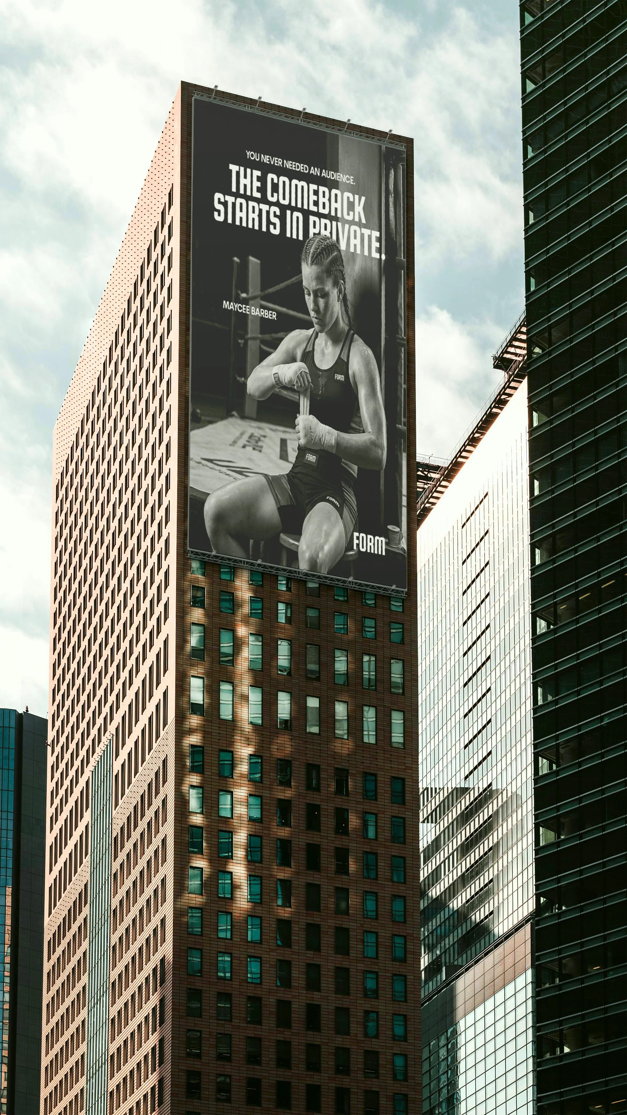 A large black and white advertisement on a tall building in an urban cityscape, featuring a female boxer tying her hand wraps, with the text 'You never needed an audience. The comeback starts in private.'