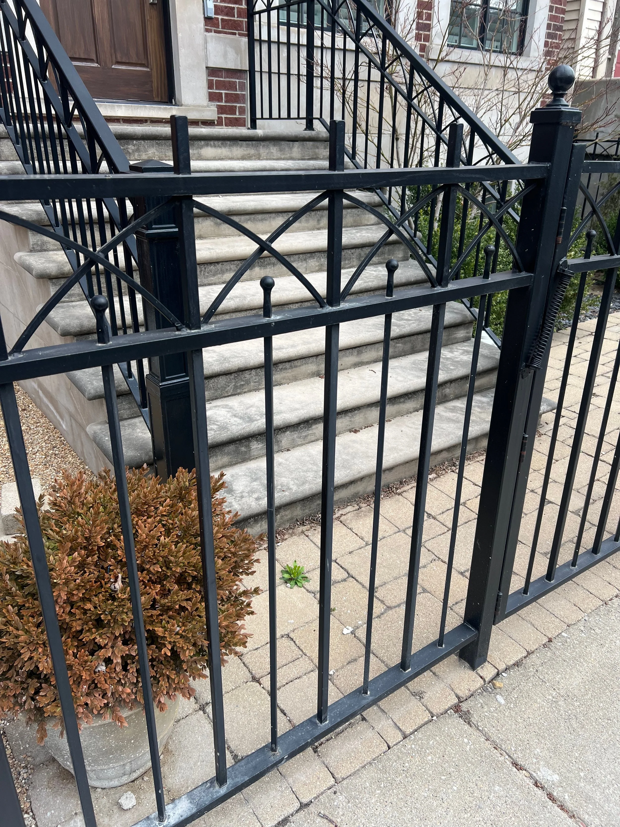 Black metal fence surrounding concrete stairs leading to a brick building entrance with a wooden door.