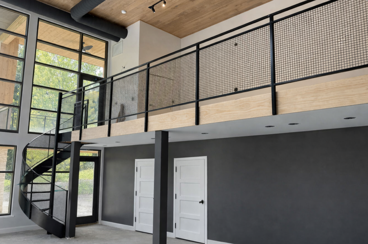 Interior view of a modern home with a spiral staircase, large windows, and a screened balcony on the upper level.