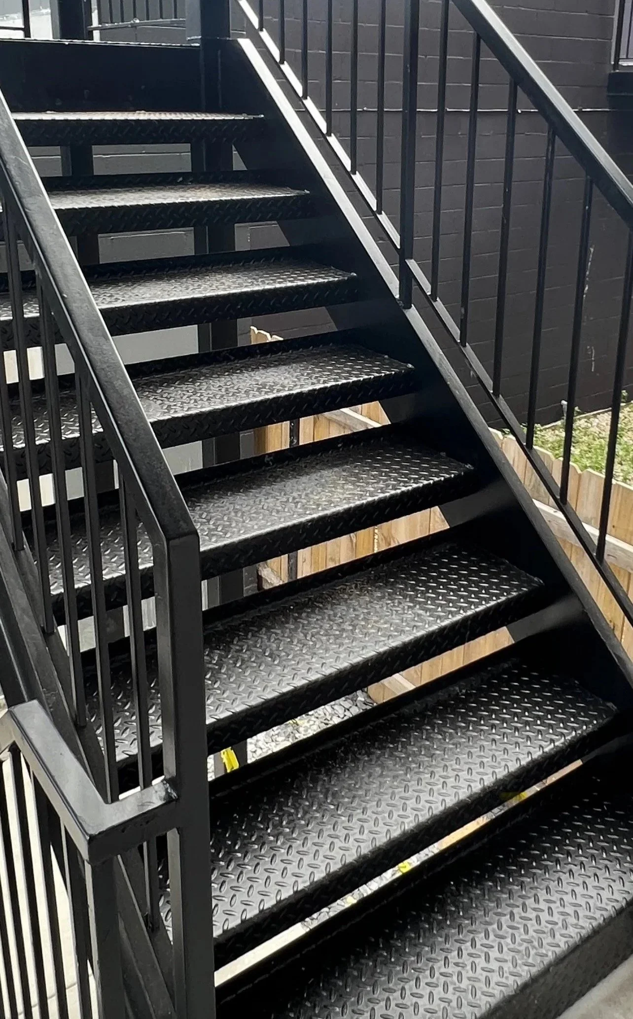 Black metal outdoor staircase with diamond plate steps and black railings, leading to an upper level.