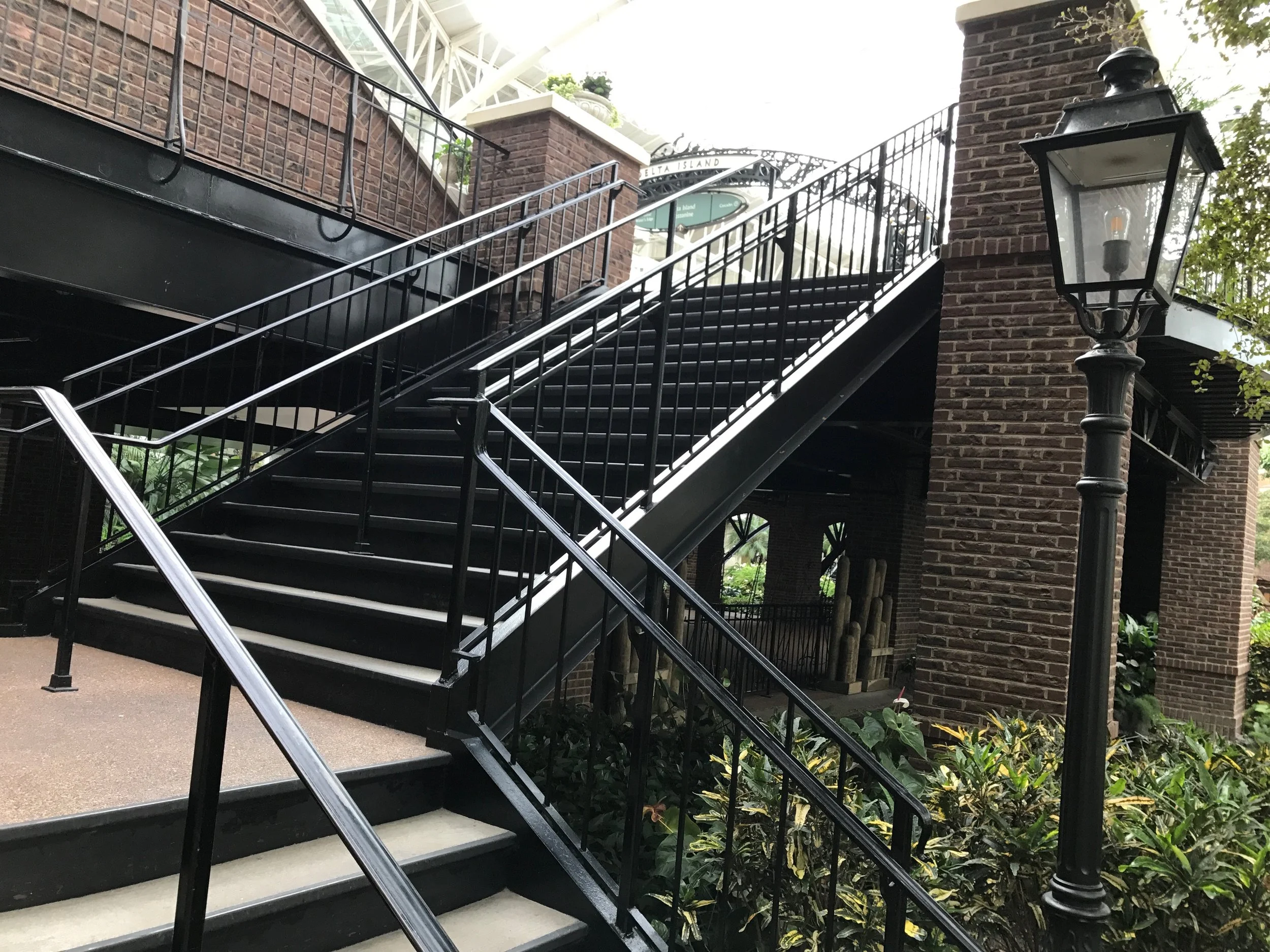Outdoor metal staircase with black railings, adjacent brick walls, and a decorative street lamp, leading to a building with a sign reading "Delta Island."