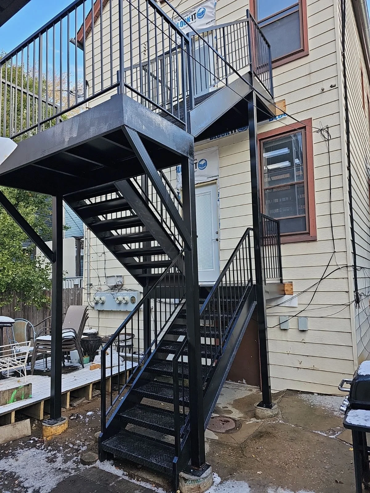 Back of a house with an outdoor black metal staircase and balcony, beige siding, and a window.