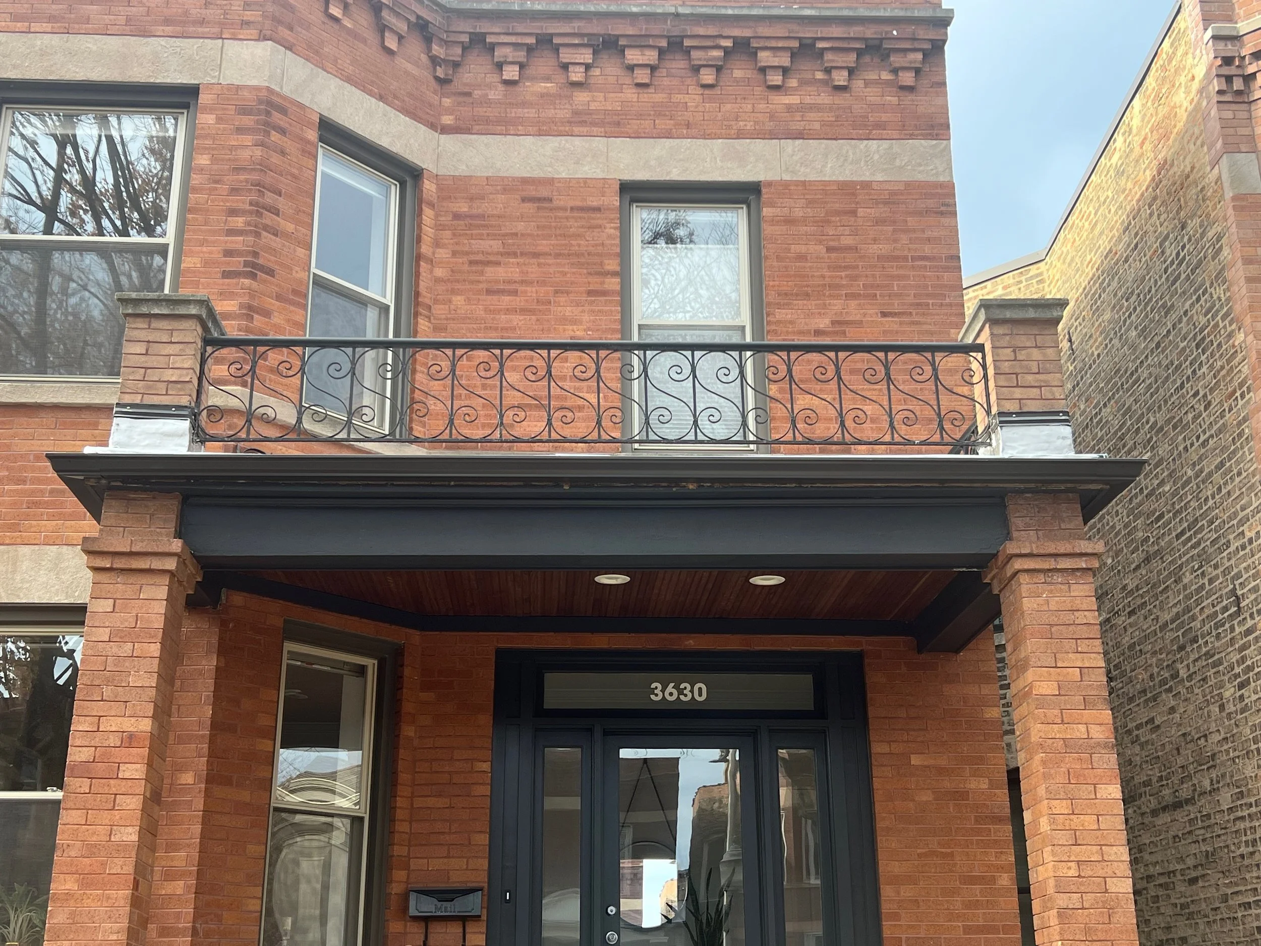 Facade of a modern brick townhouse with a small balcony, black wrought iron railing, and a black front door with the house number 3630.
