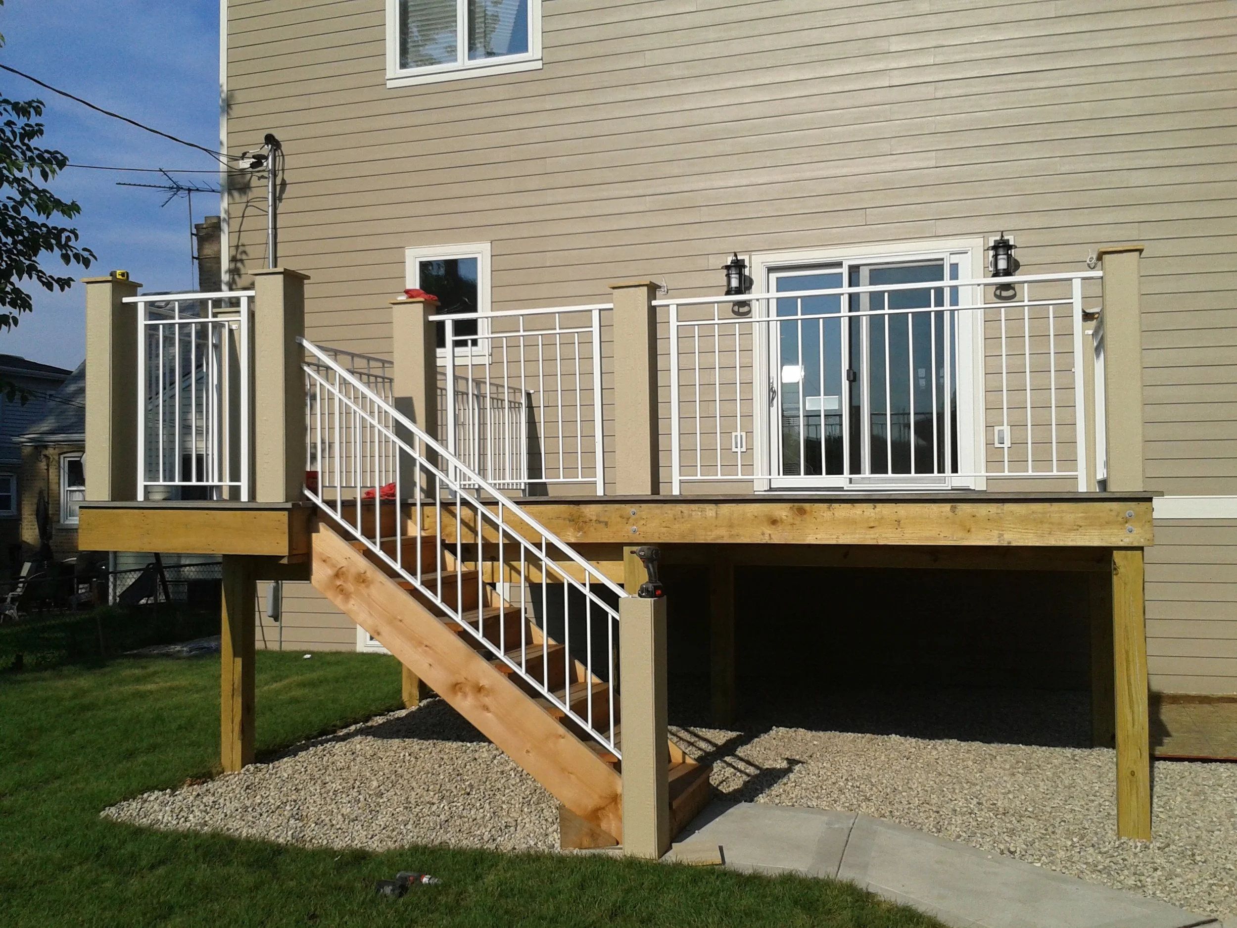 A house with beige siding and a screened sliding glass door balcony with a white railing under construction, with stairs leading up to it and outdoor lights on the wall.