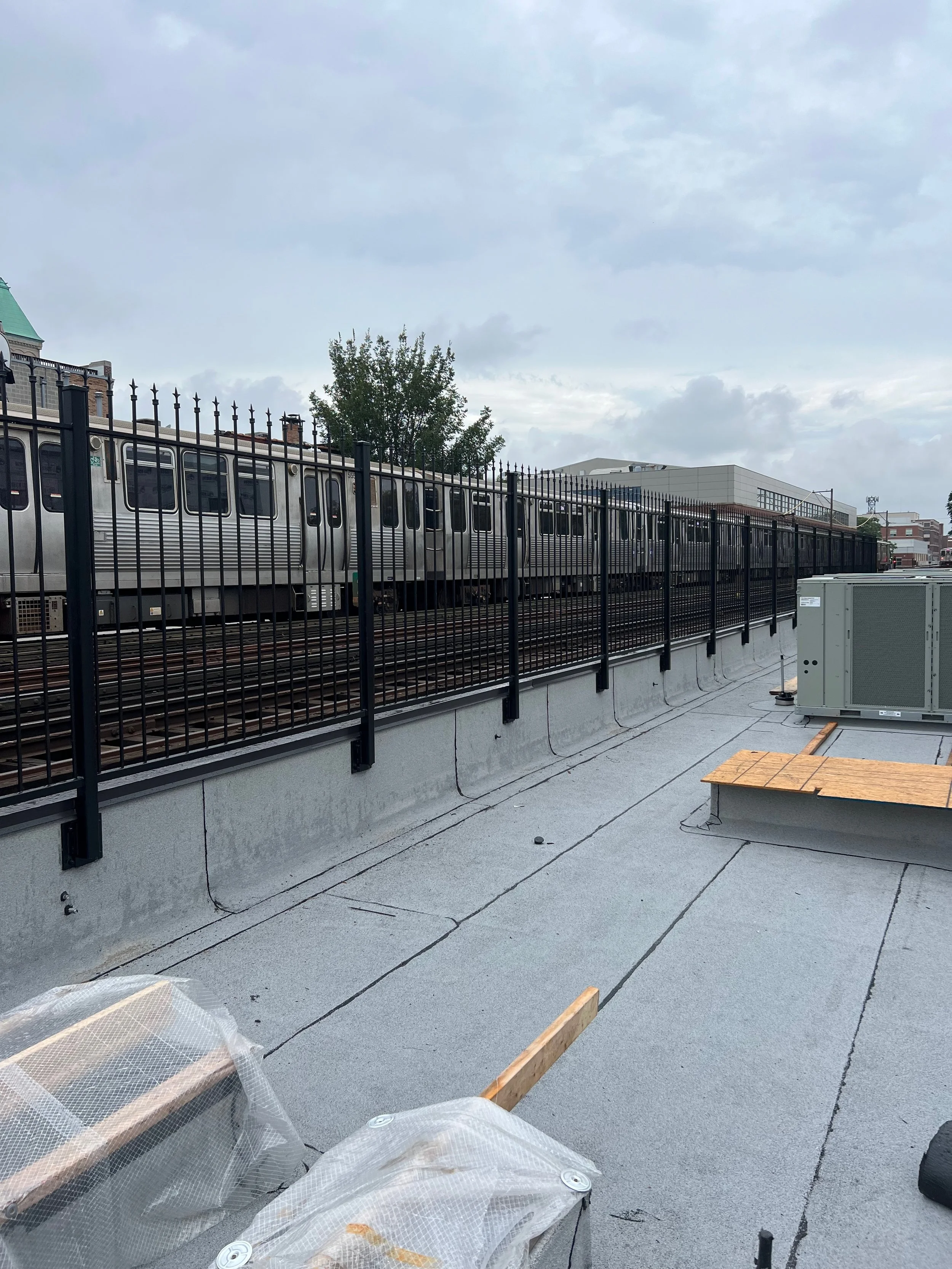Construction site on a rooftop with protective fencing, a bench, and construction materials, under a cloudy sky.