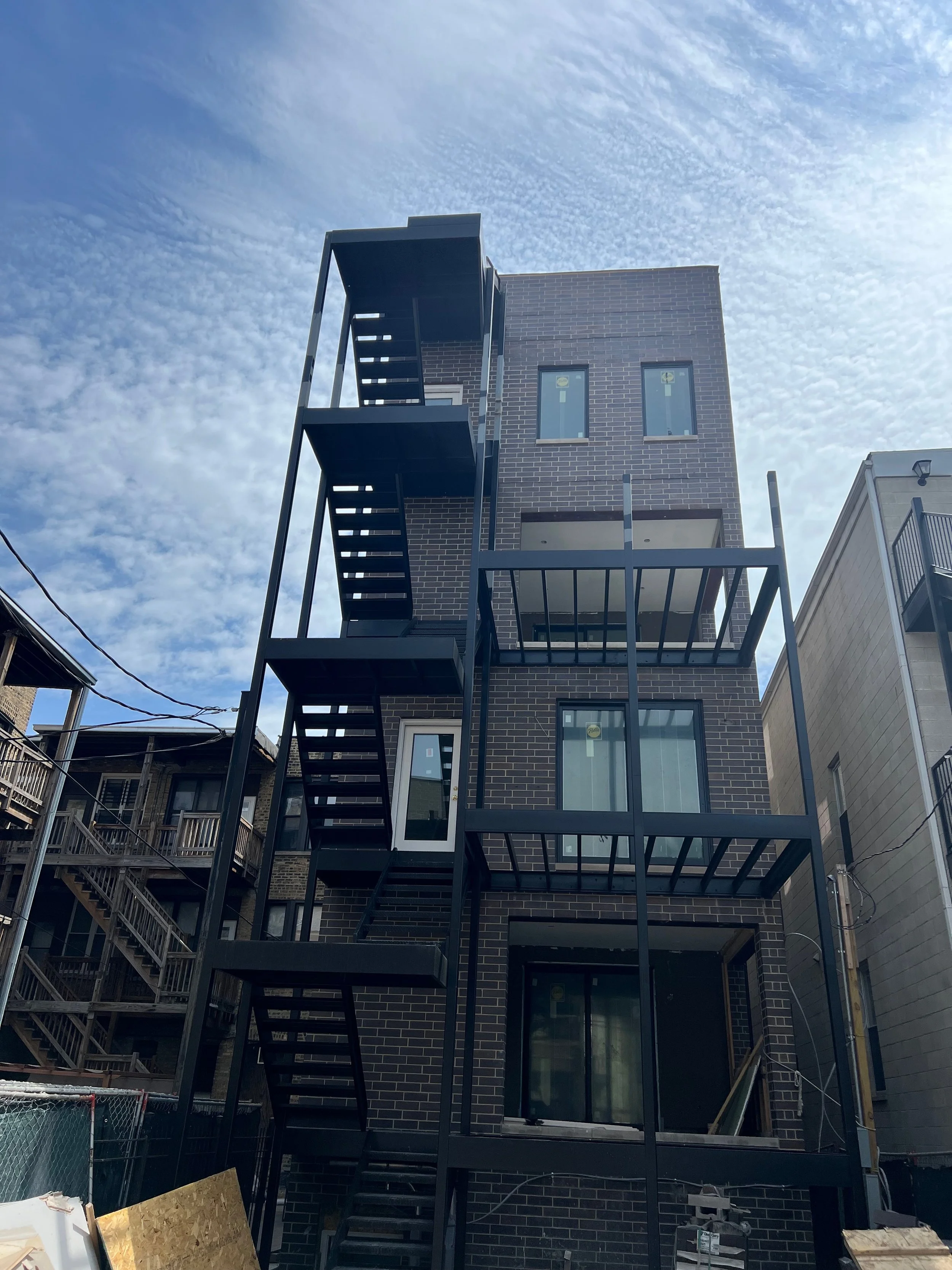 Building under construction with black exterior and fire escape staircase