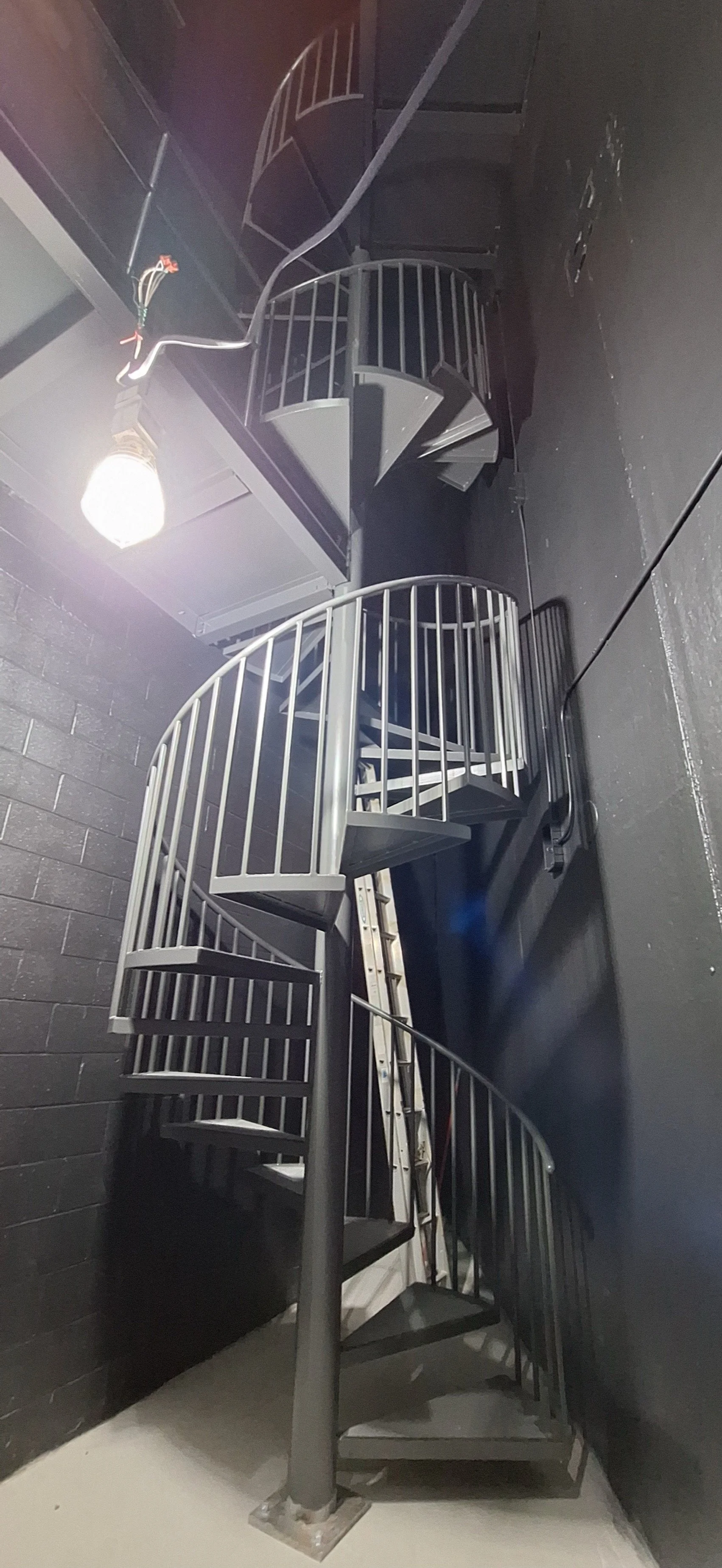 Metal spiral staircase with black railings in an industrial-style space.