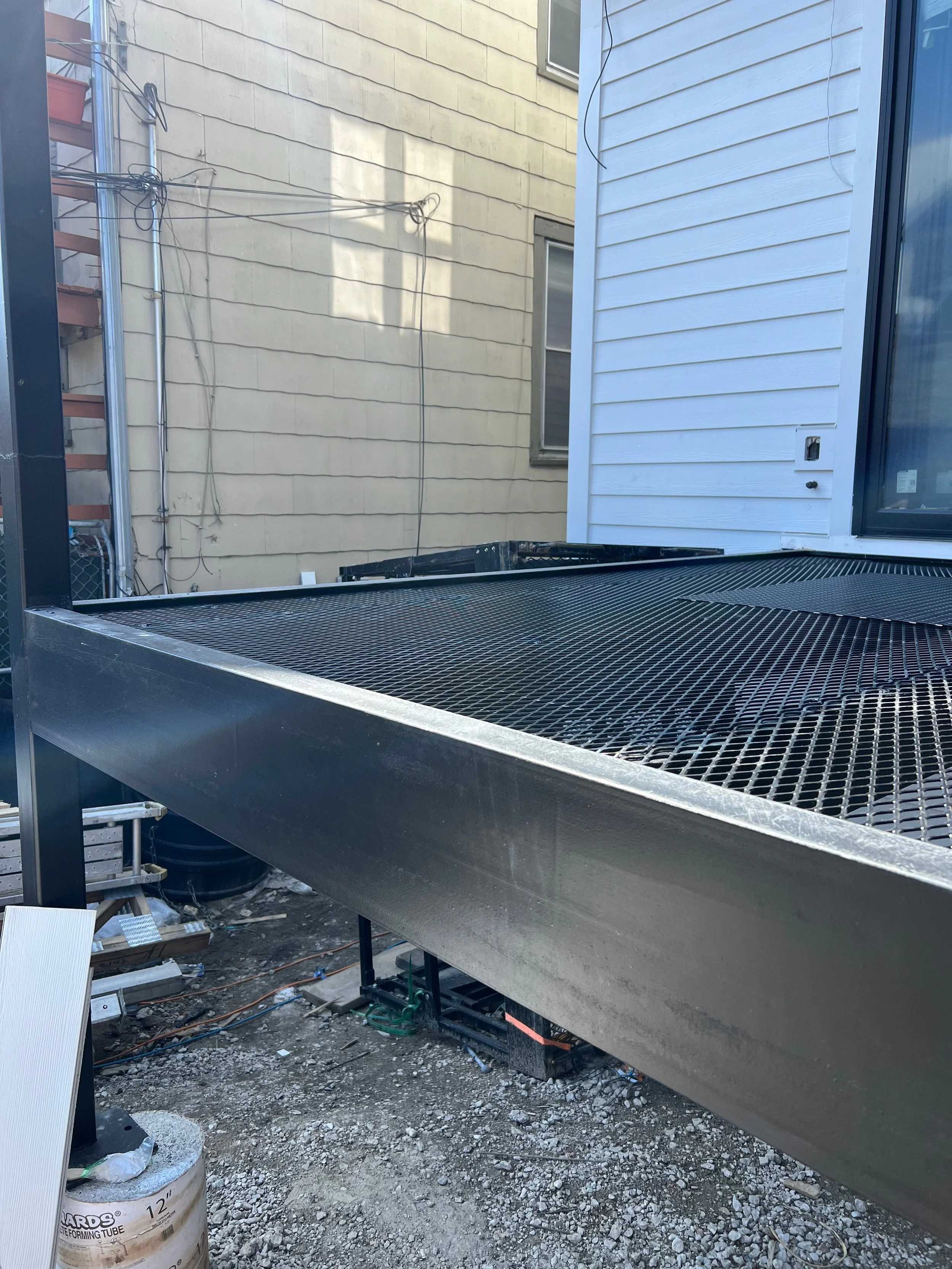 Construction site with metal platform, PVC pipes, and wires against the walls of a house.