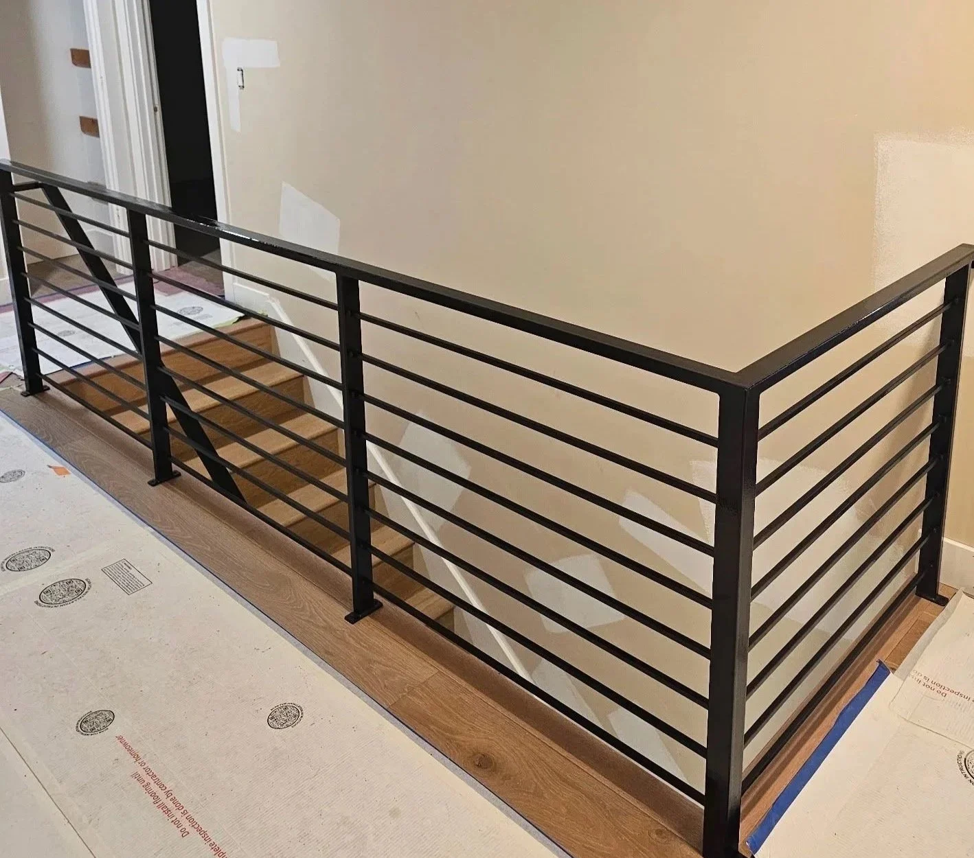 A black metal railing installed on a wooden floor at the edge of a staircase or balcony in a house interior.