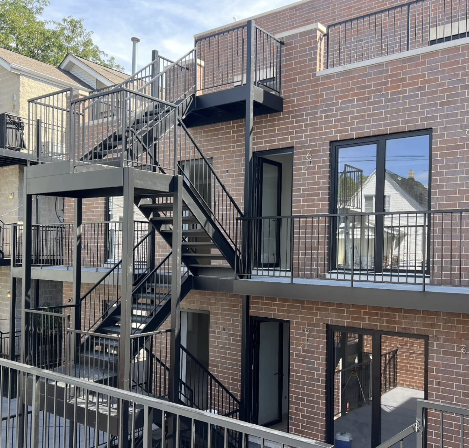 The image shows the back exterior of a brick apartment building with several metal fire escape staircases and landings.