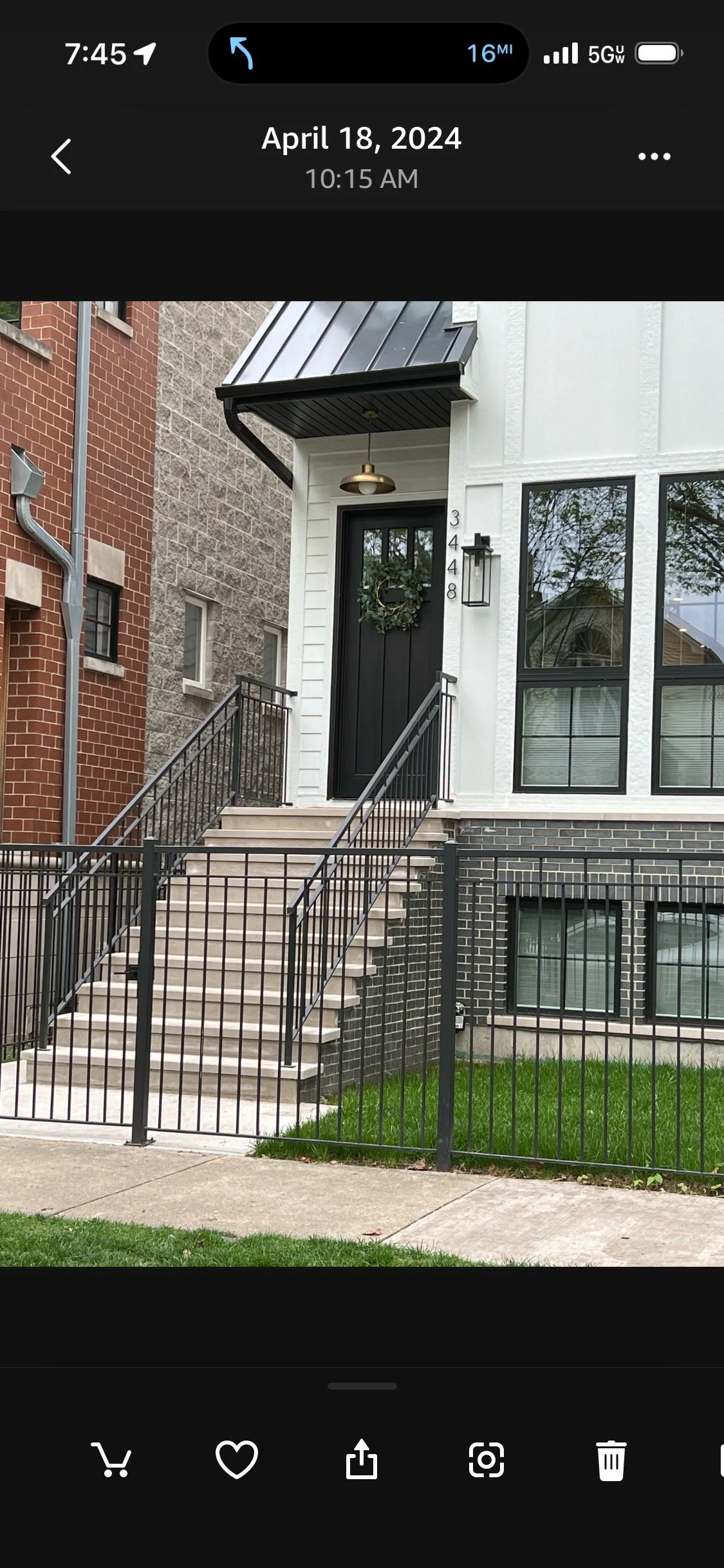 Front view of a modern house with stairs leading up to a black door decorated with a wreath, white siding, large windows, and a black metal fence and railing.