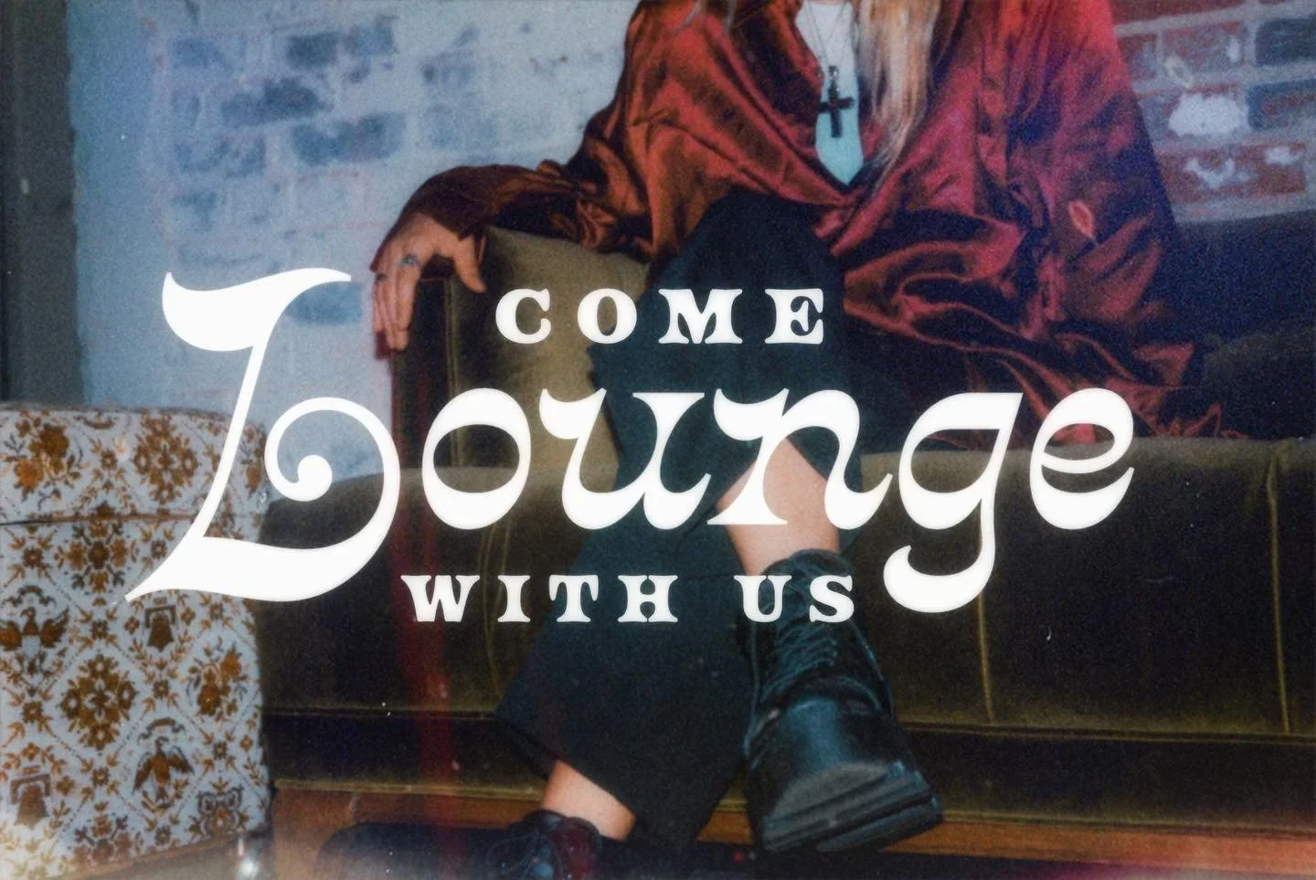 A person dressed in a red velvet blazer, black pants, and boots, sitting on a vintage green couch with crossed legs, with text overlay that says 'Come Journey With Us'.