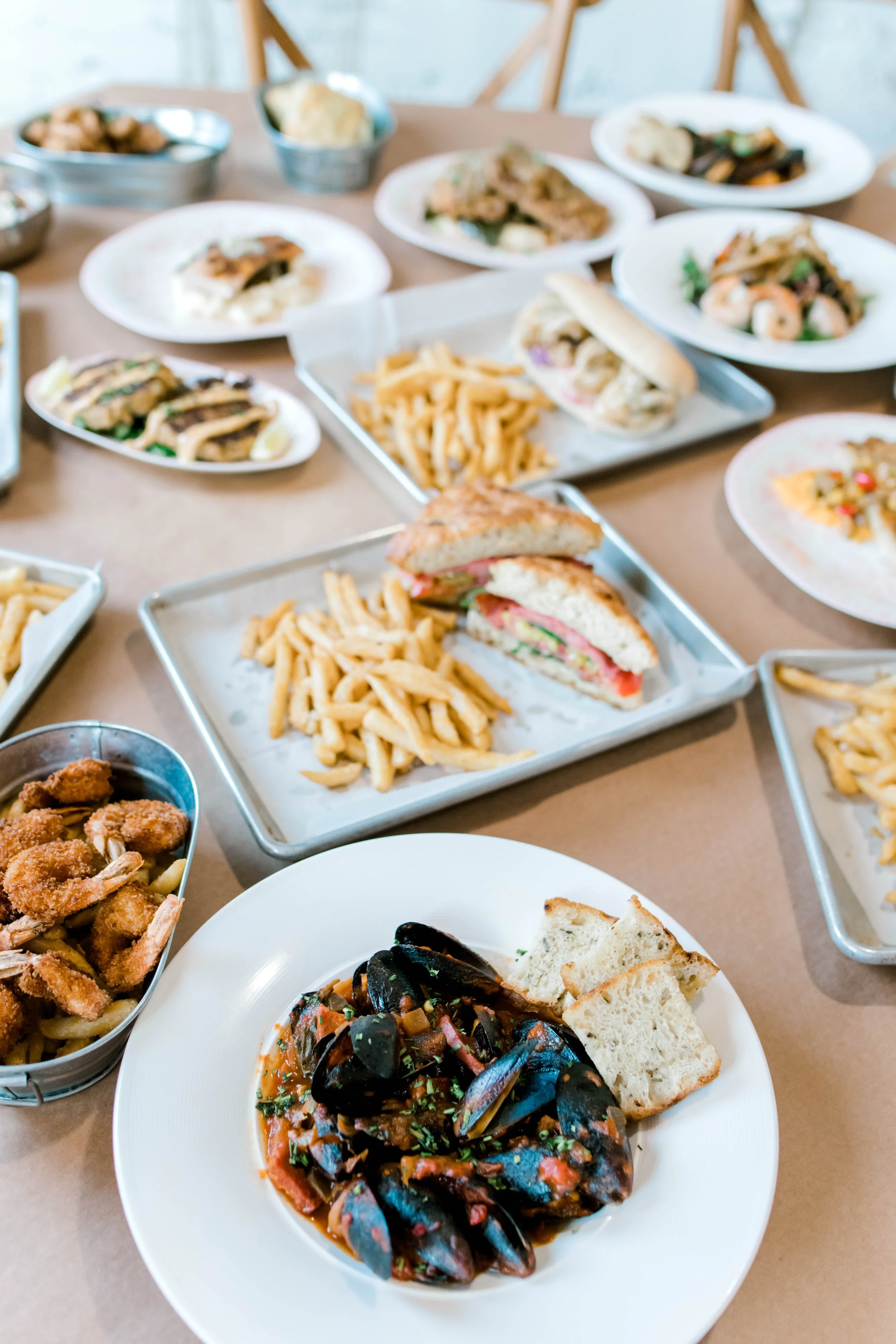 Various plates of food on a dining table, including a seafood stew, French fries, sandwiches, pasta, fried shrimp, and other dishes.
