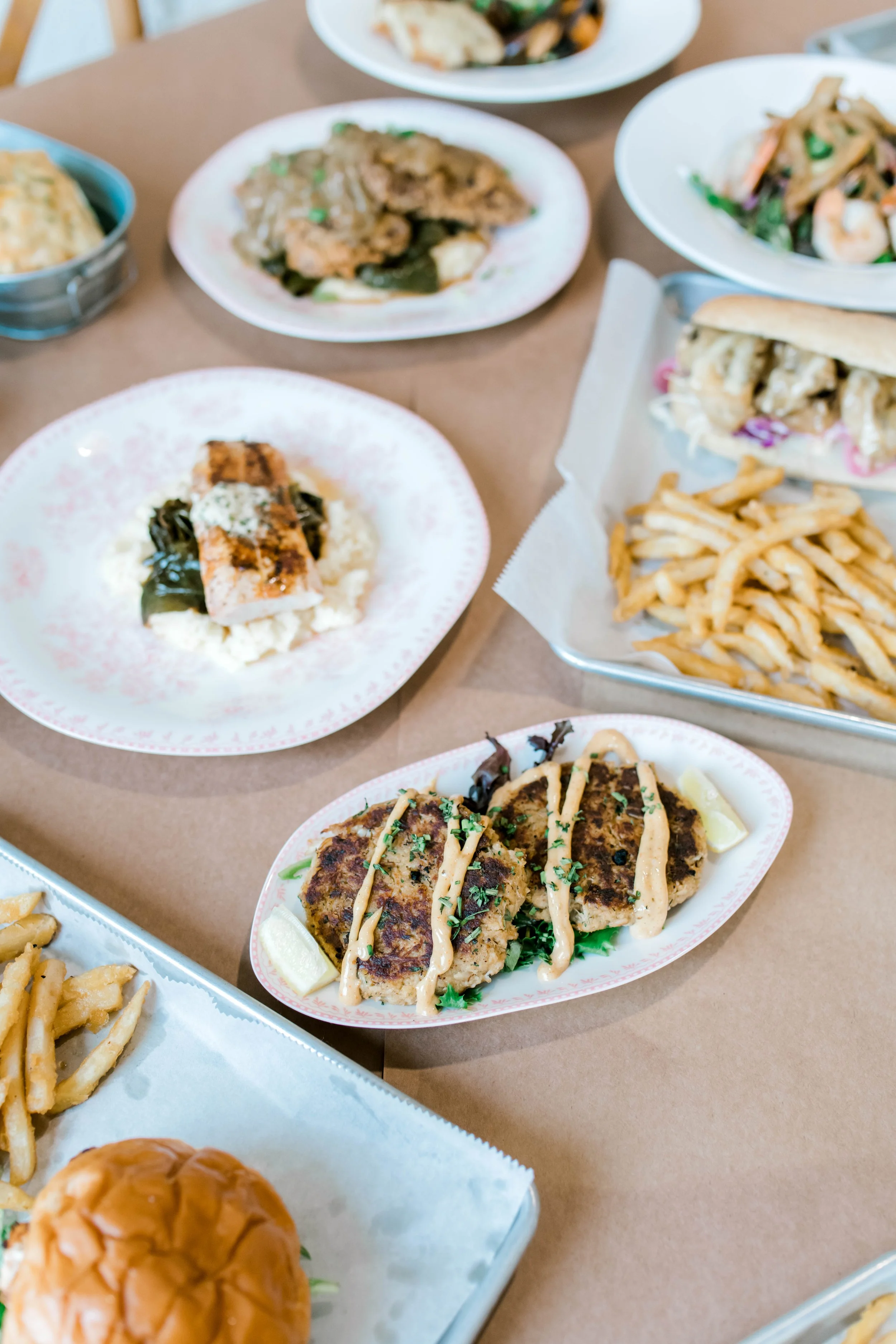 Assorted plates of Asian cuisine including fried chicken, stir-fried vegetables with shrimp, fried rice, and French fries on a table.