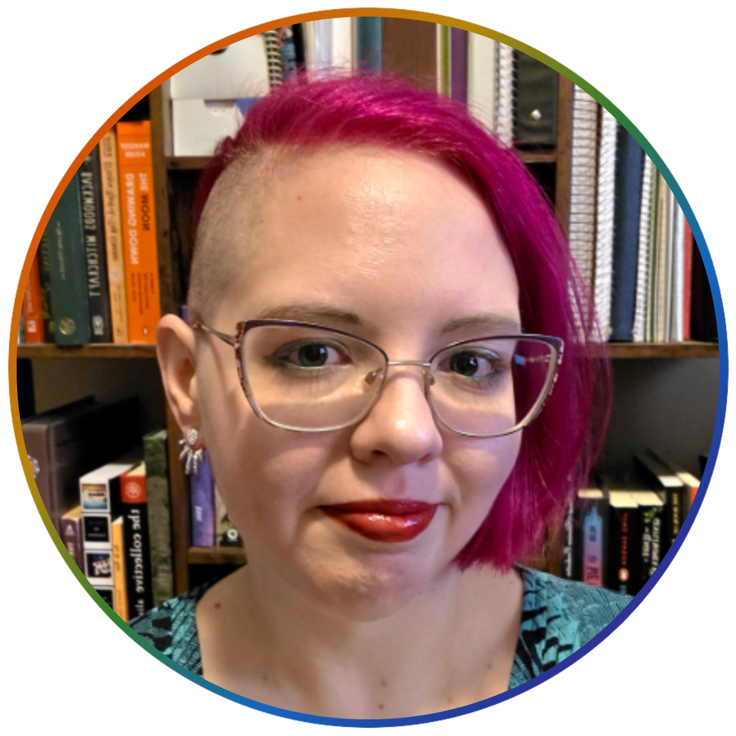 A woman with pink hair, glasses, and earrings poses for a photo in front of a bookshelf.