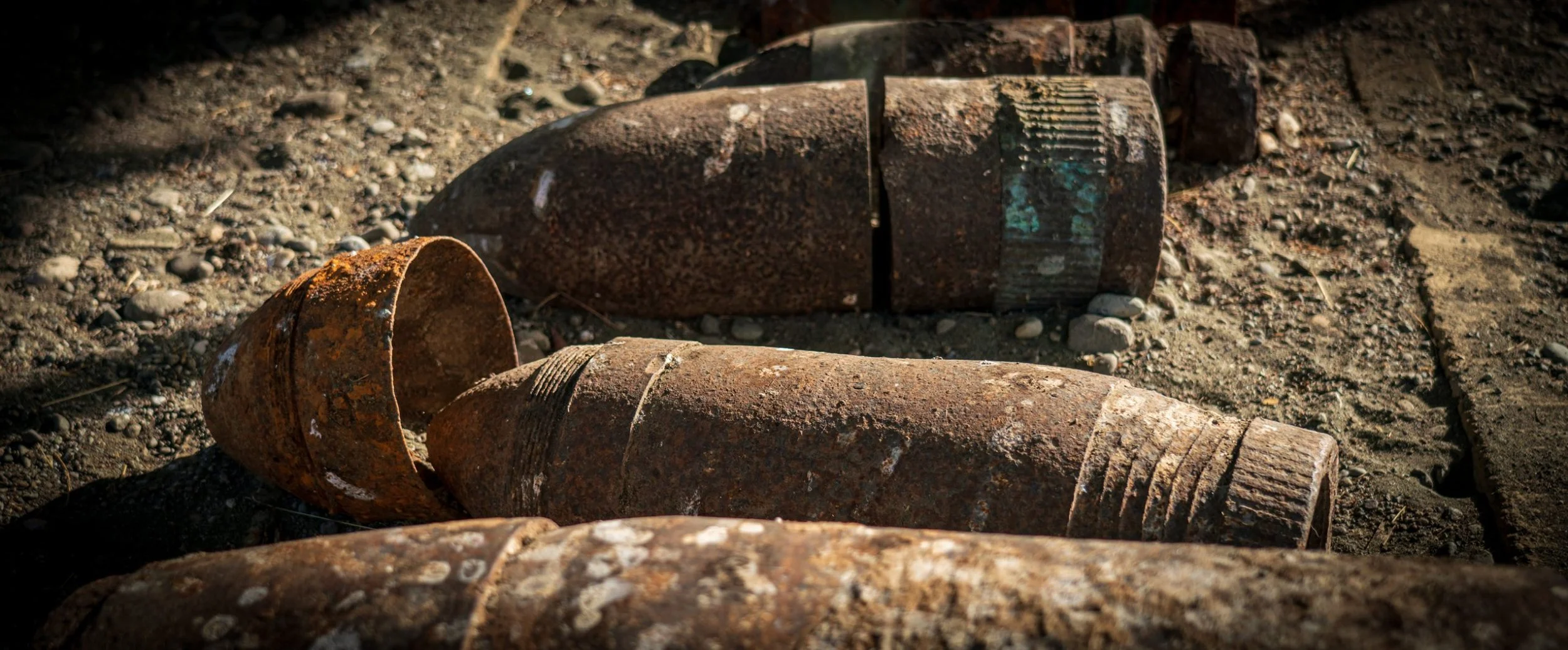 Rusty, abandoned bombs lying on dirt ground.
