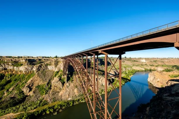 A large bridge over a canyon with a river below, under a clear blue sky.