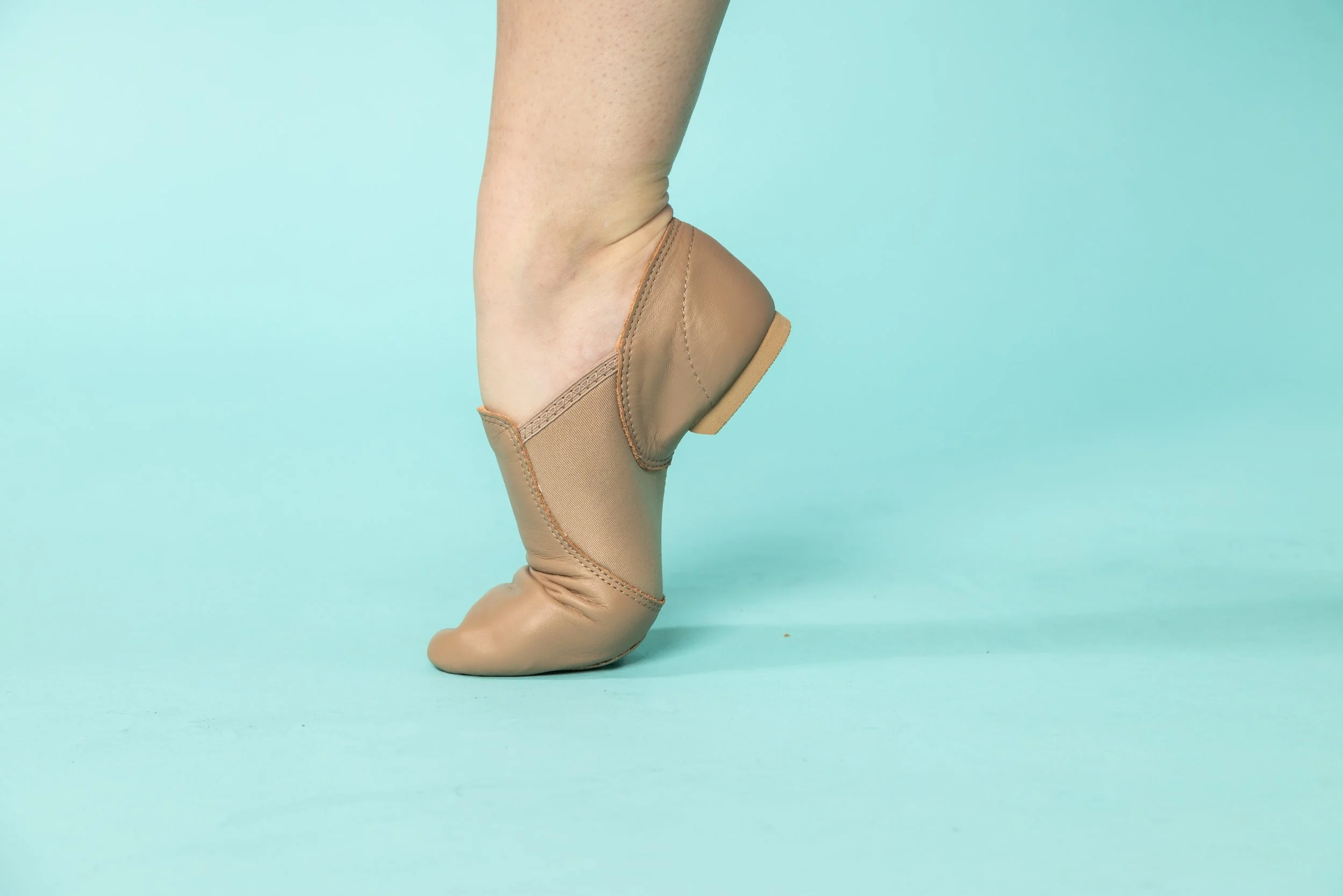A ballet dancer's leg in a beige pointe shoe against a light blue background.