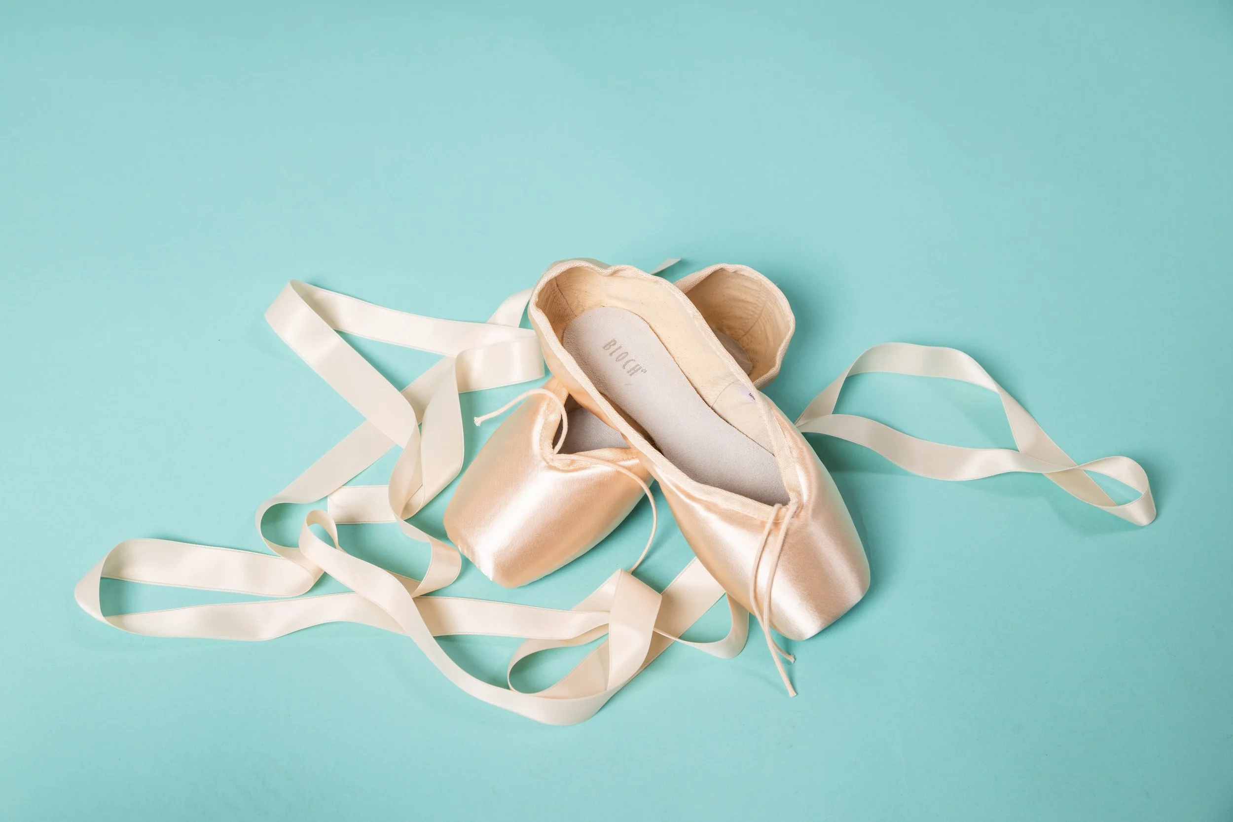 Pink ballet pointe shoes with satin ribbons on a light blue background.