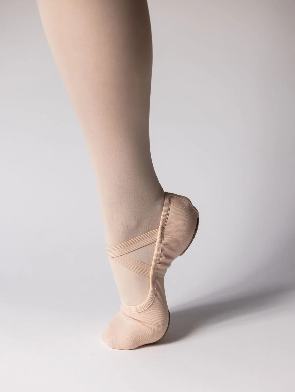 A ballet dancer's foot in a ballet flat and pink tights, standing on toes.