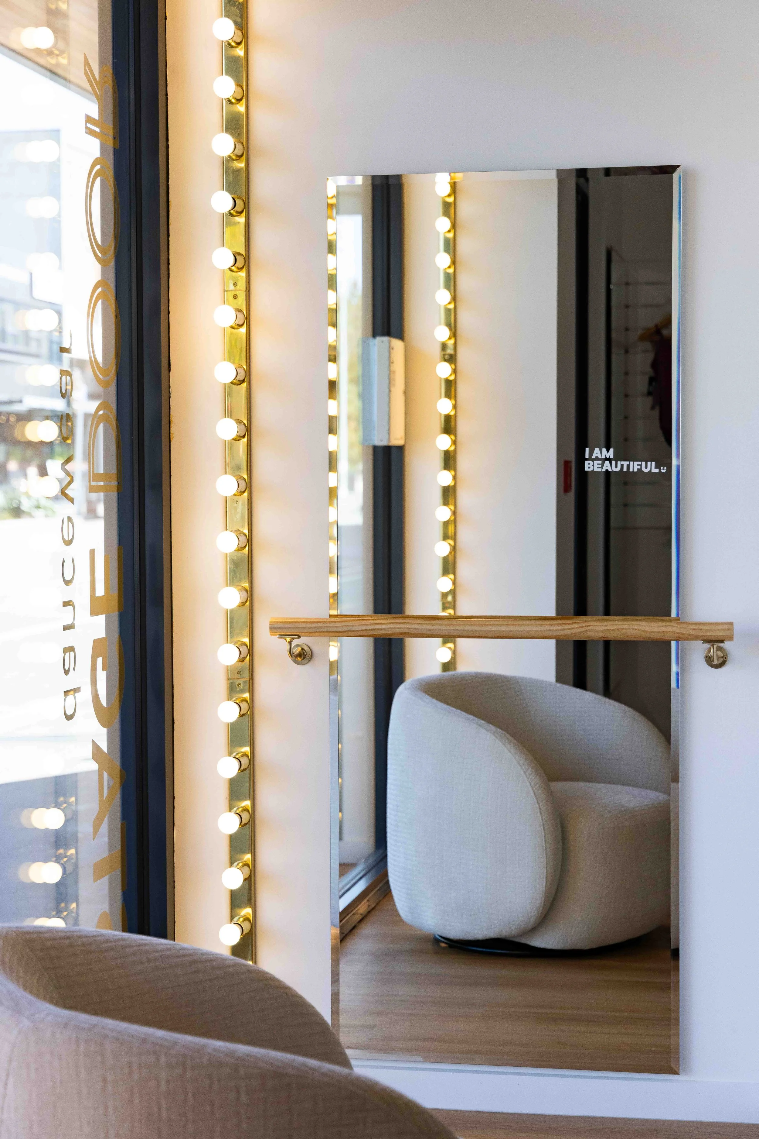 A mirror reflecting a chair and a partial view of a room with light-colored walls, a wooden floor, and decorative string lights.