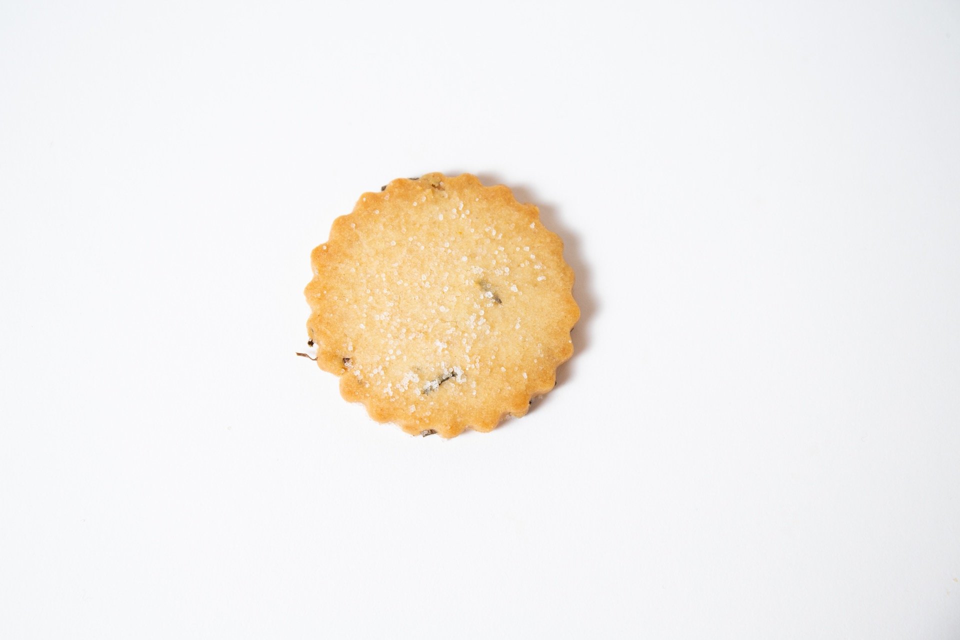 A round cookie with scalloped edges, sprinkled with coarse sugar, on a white background.