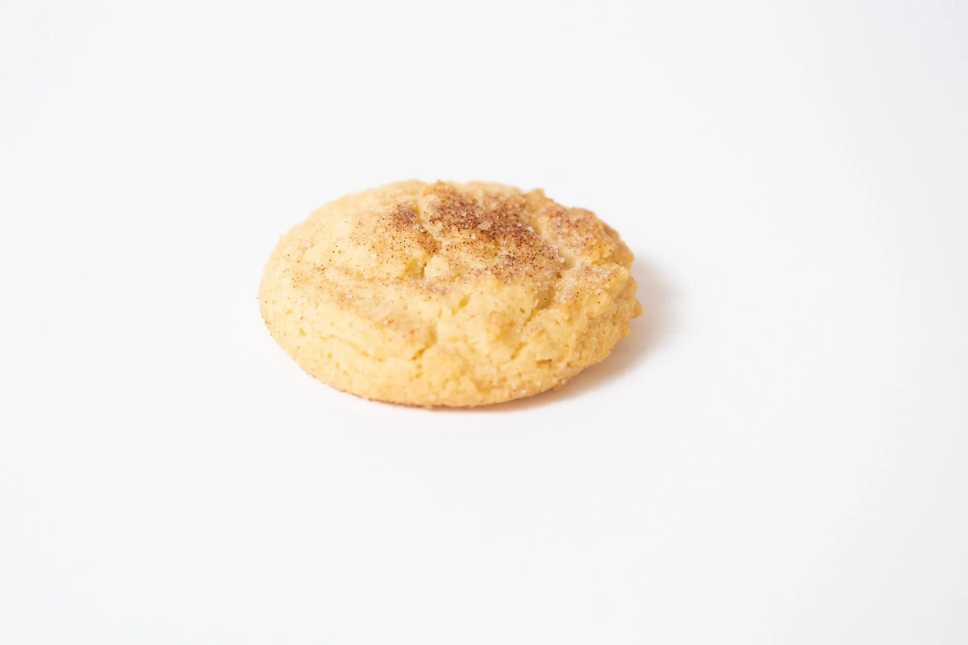 A round cookie with a slightly cracked surface, sprinkled with cinnamon on top, placed on a white background.