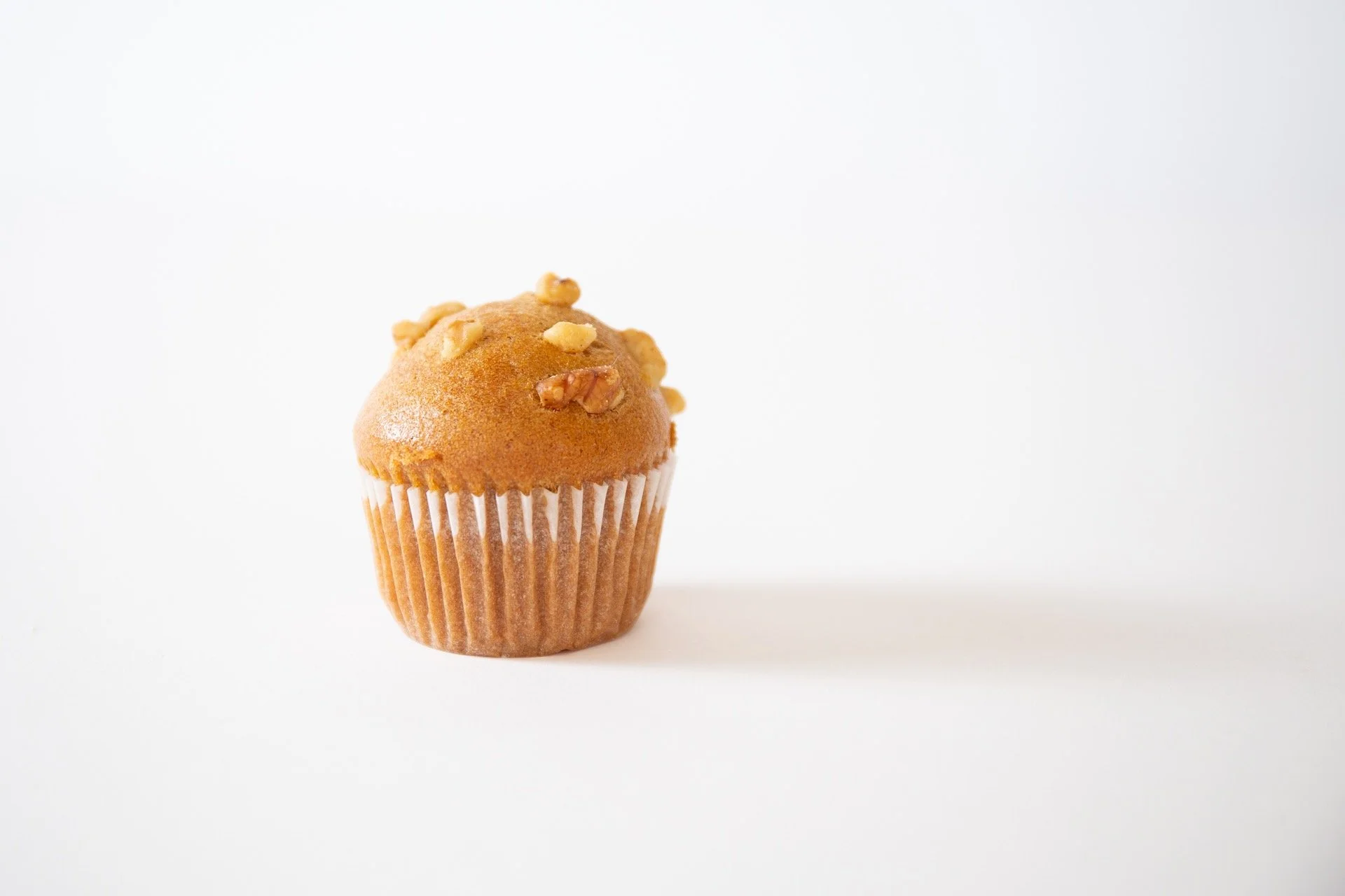 A single muffin with chopped nuts on top sits in a paper liner on a white background.