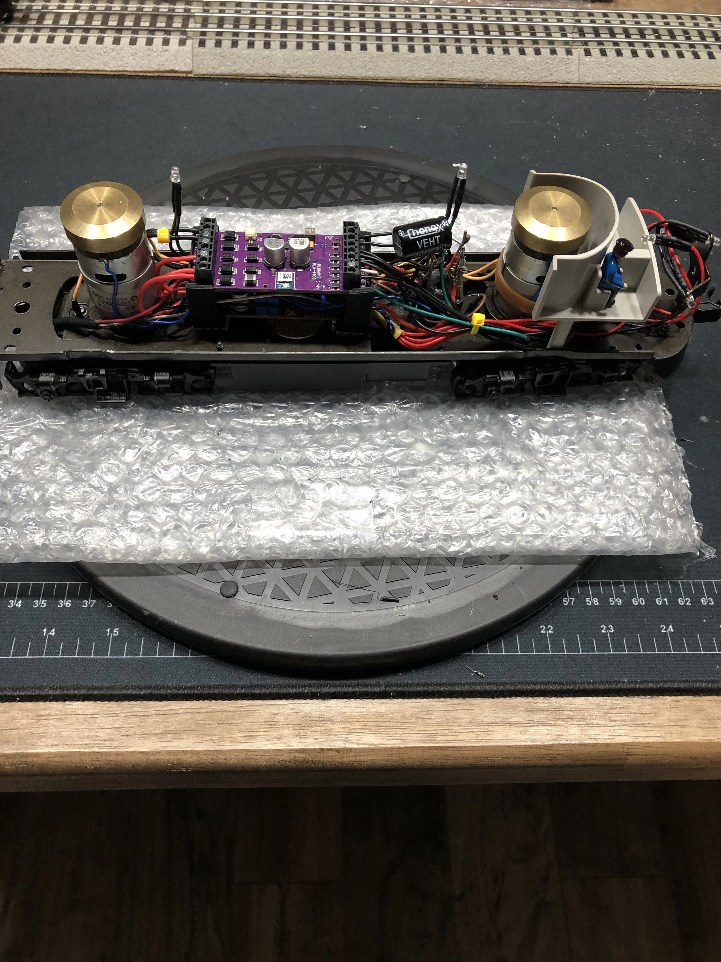 Model train chassis with two motor units, wiring, and electronic components on a work surface.