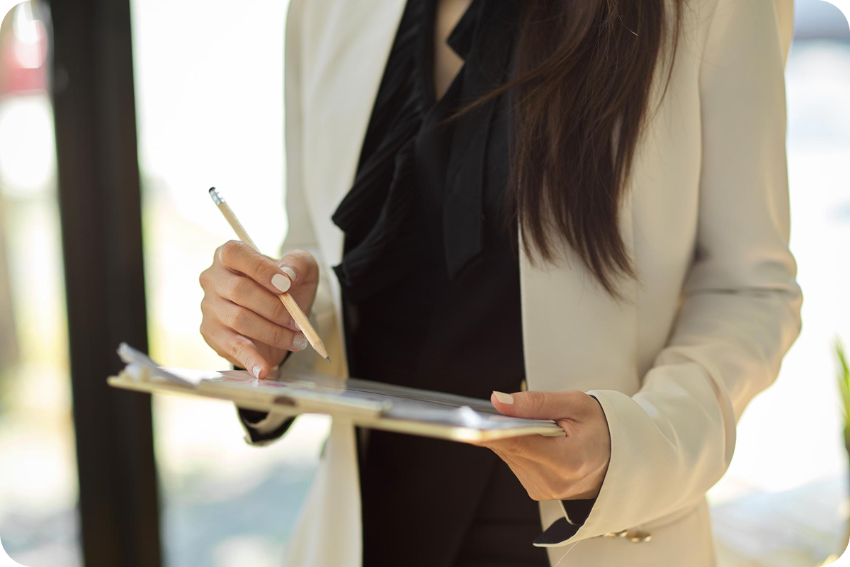 A woman in a white blazer holding a clipboard and writing with a pencil.
