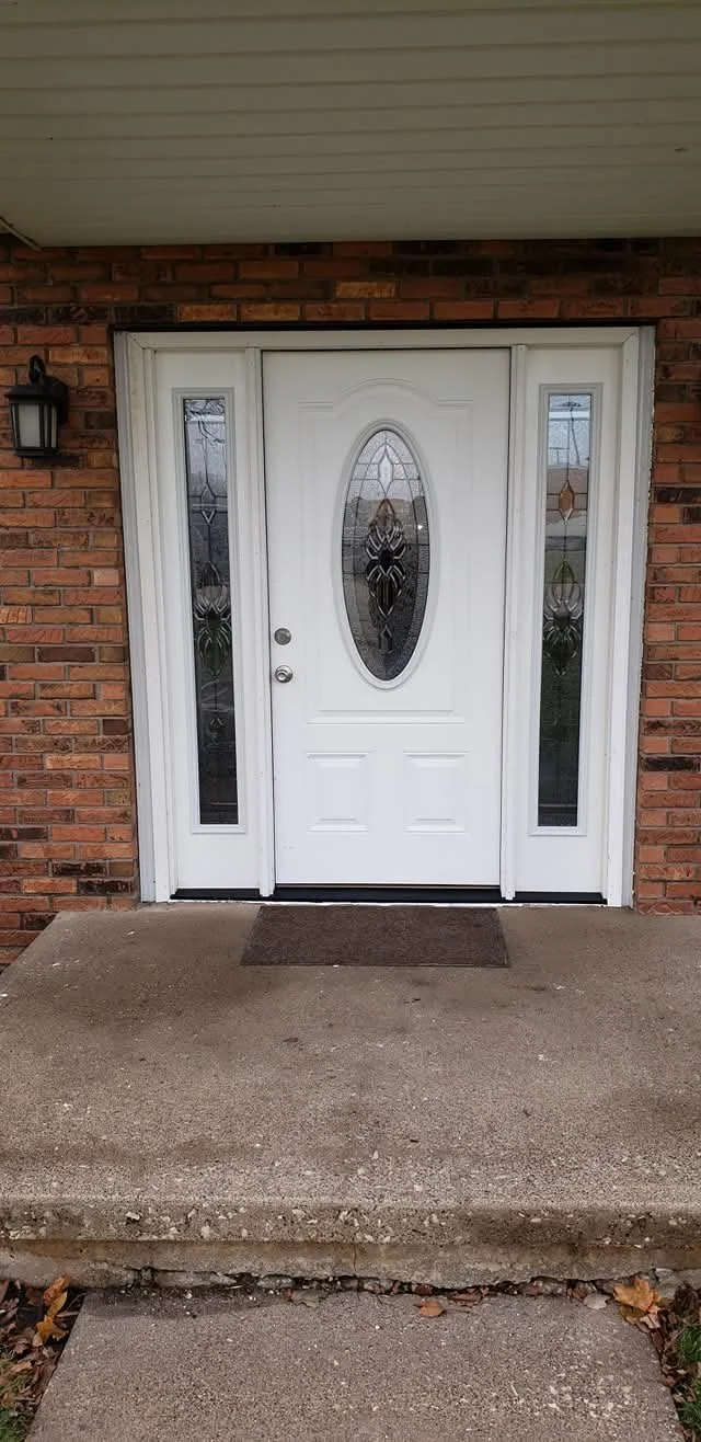 Front door of a house with glass panels and a white frame, brick exterior wall, and a porch with concrete steps.