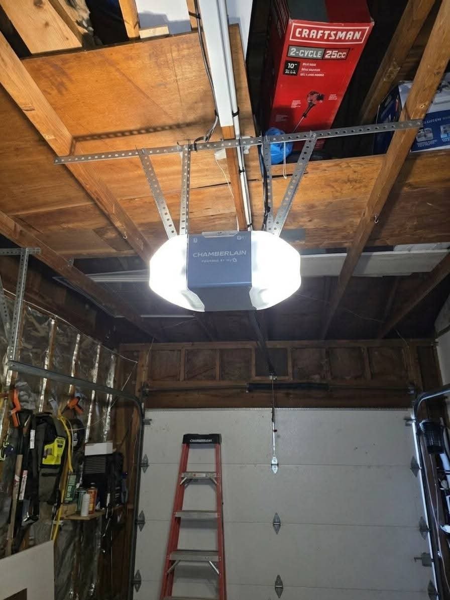 Garage ceiling with a garage door opener, a ladder, and a red box of a Craftsman 2-cycle 25cc string trimmer, with tools and supplies on the garage wall.