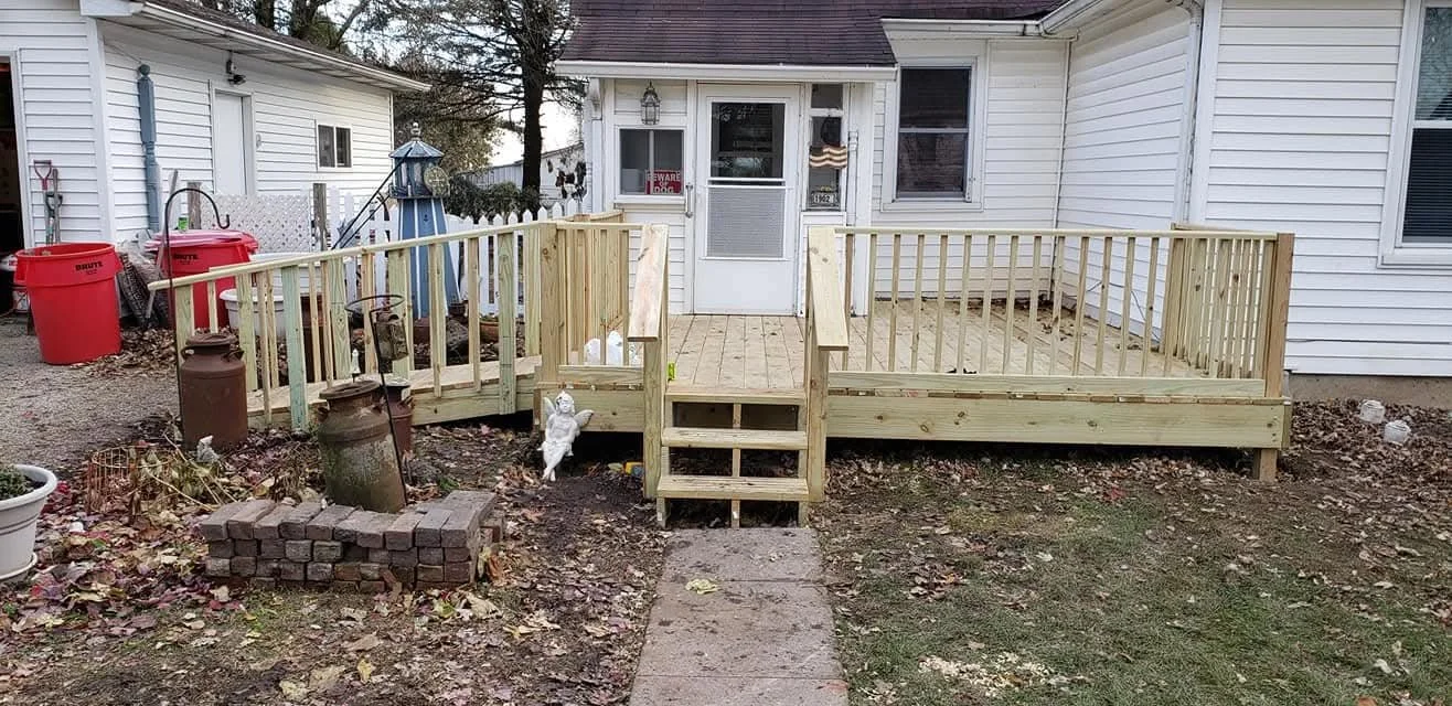 A newly built wooden deck attached to a white house with steps leading up to it and a railing around it.