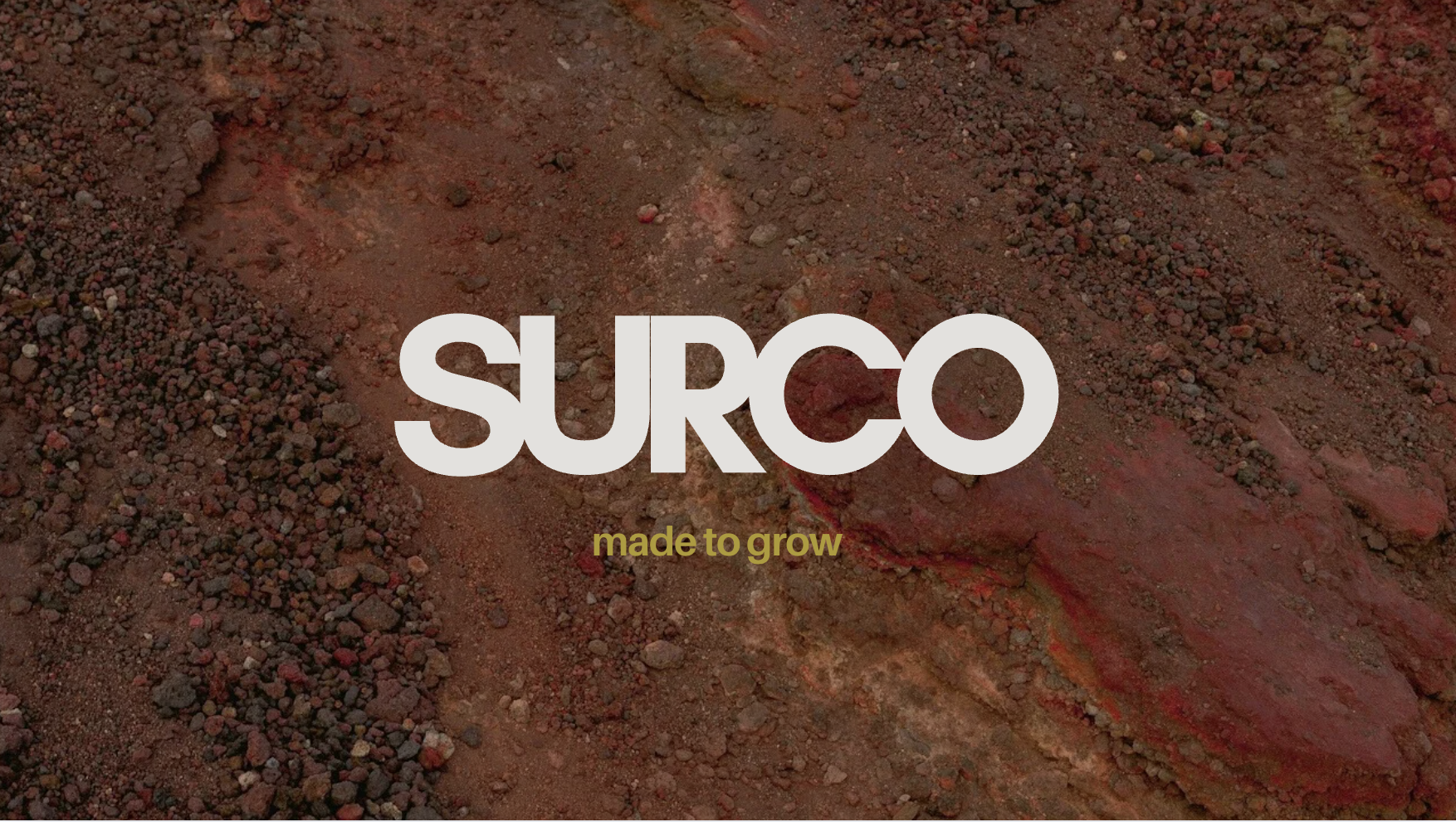 Close-up of red dirt soil with the white text "SURCO" and yellow text "made to grow" over it.