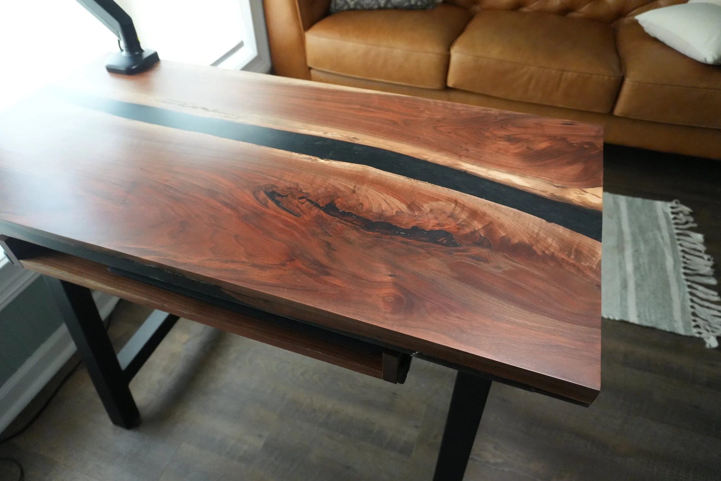 A wooden table with a black inlay in the center, positioned in a room with a sofa and a window nearby.