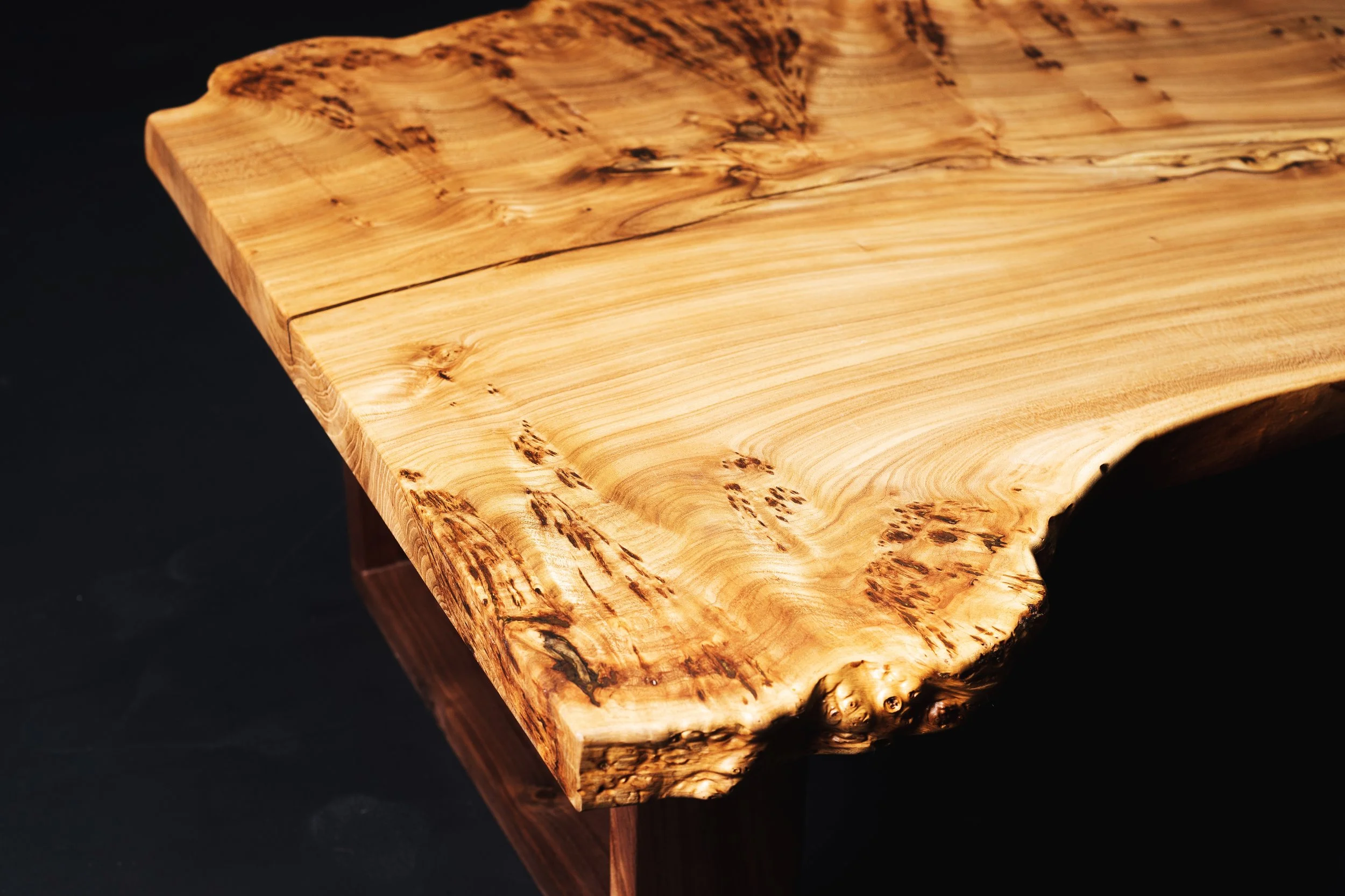Close-up of a polished custom wooden slab table with natural wood grain and knots, set against a black background.