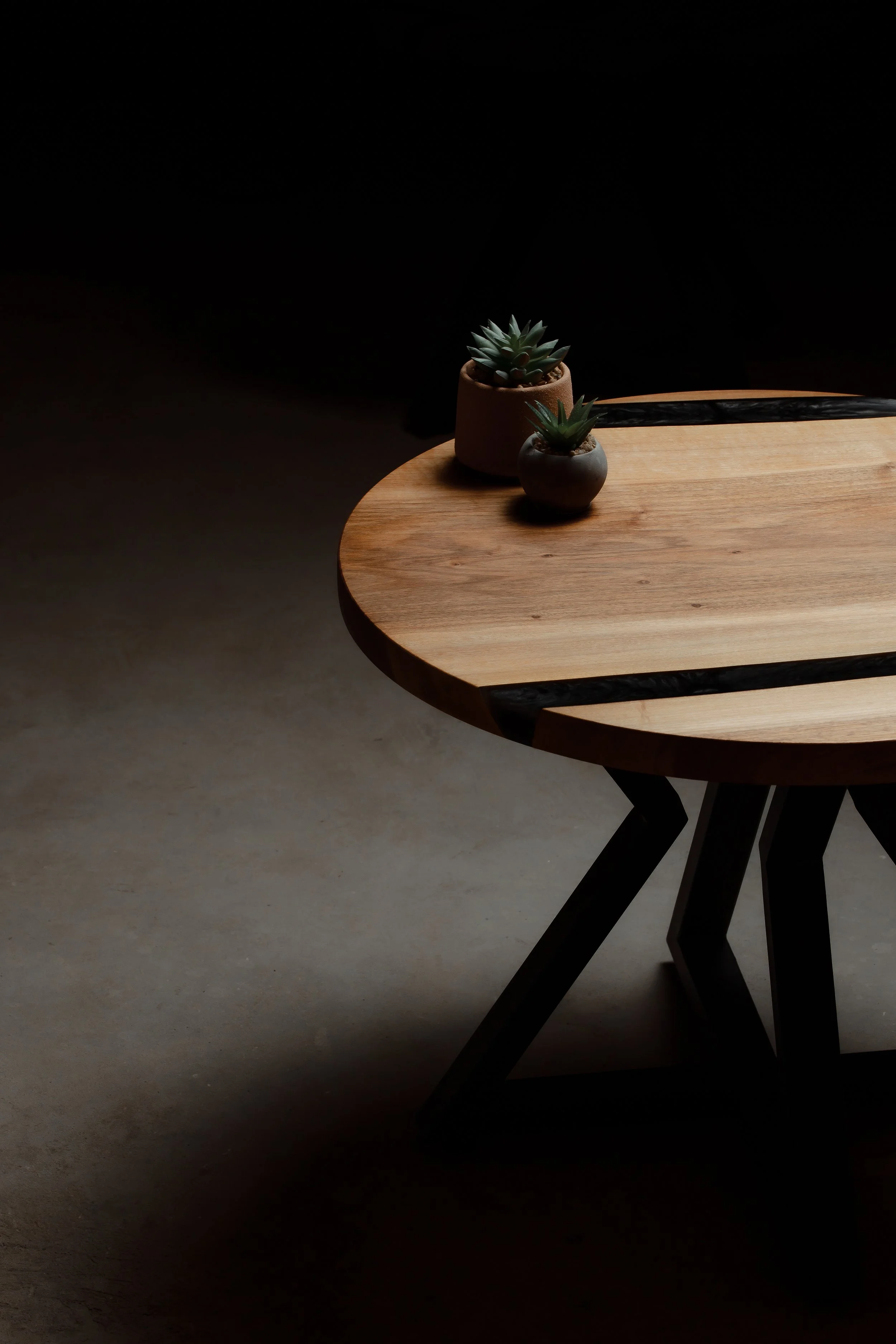 A wooden table with black metal legs, with two small potted succulent plants on top, set against a dark background.