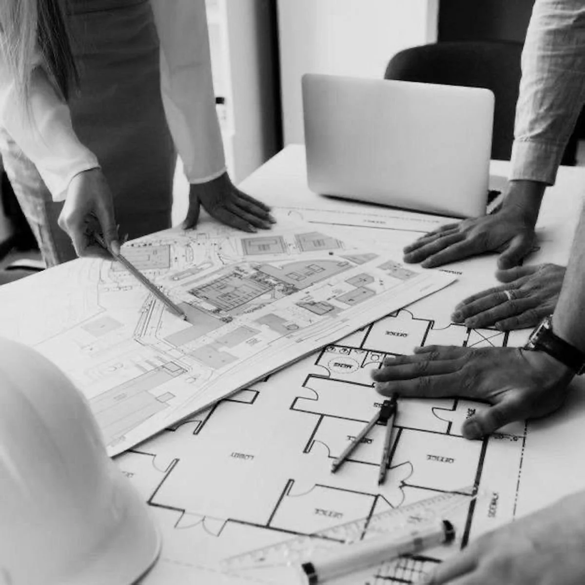 Two people in casual clothing examine architectural or engineering blueprints on a table, with a scale model of a building in the foreground.
