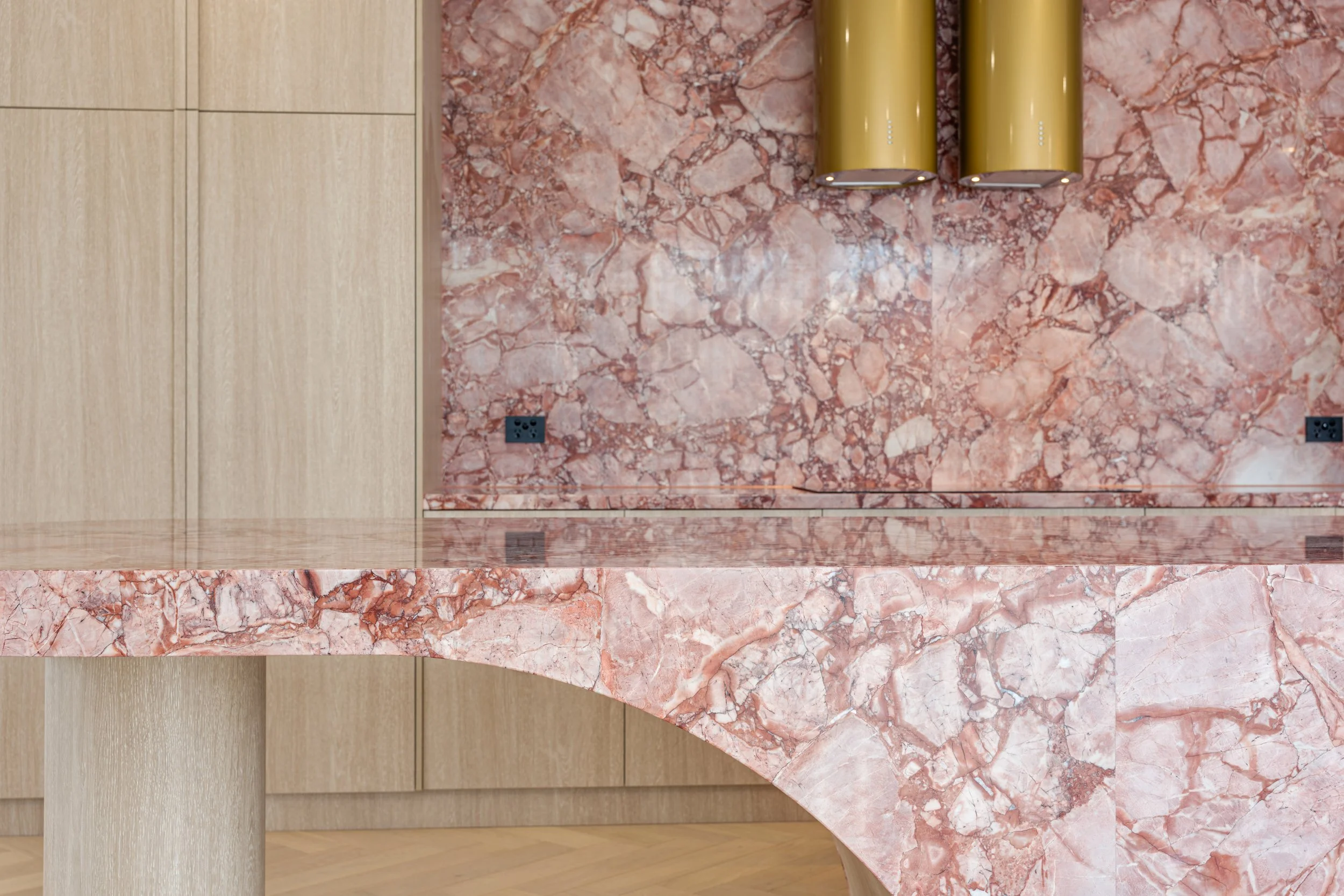 Pink marble wall with two yellow cylindrical pendant lights hung beside each other, an electrical outlet on the lower left, and wooden paneling on the left side.