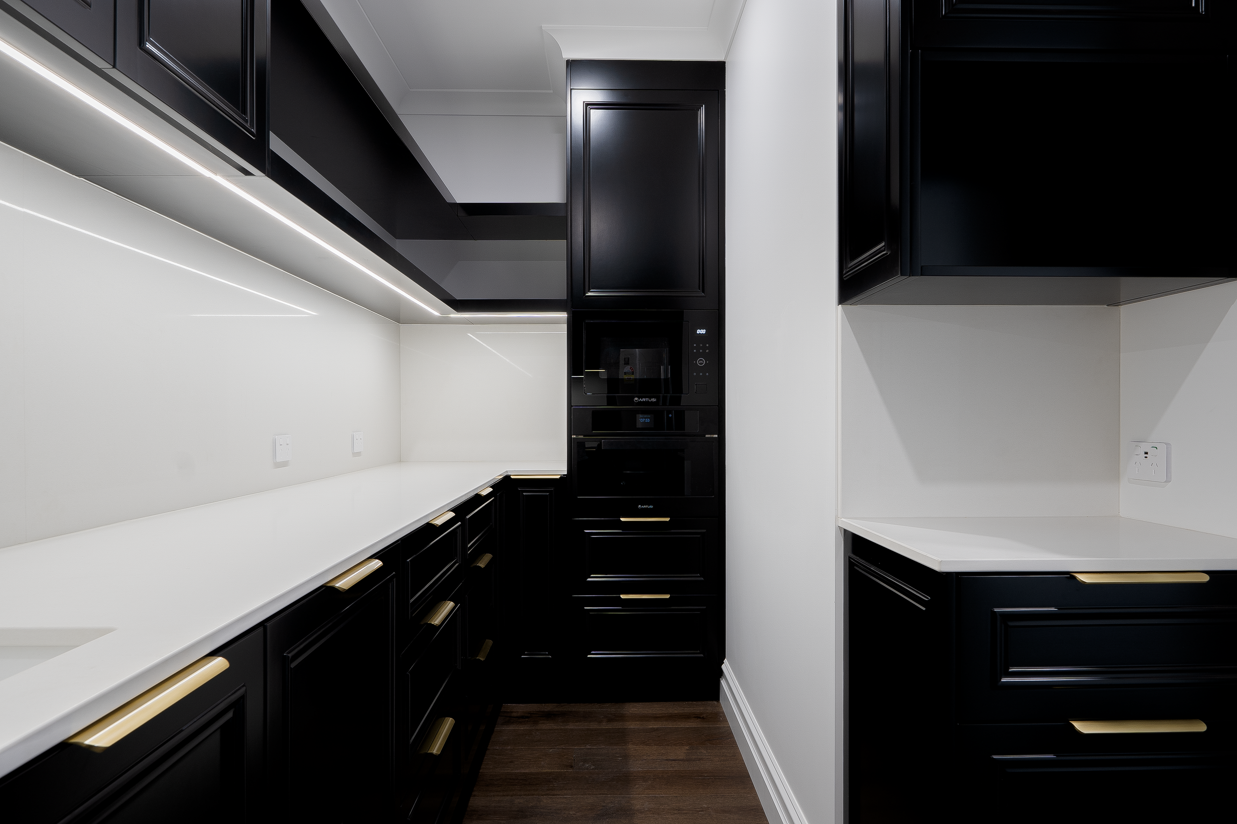 Modern black and white kitchen with black cabinets, white countertops, built-in oven, microwave, and dark hardwood floors.