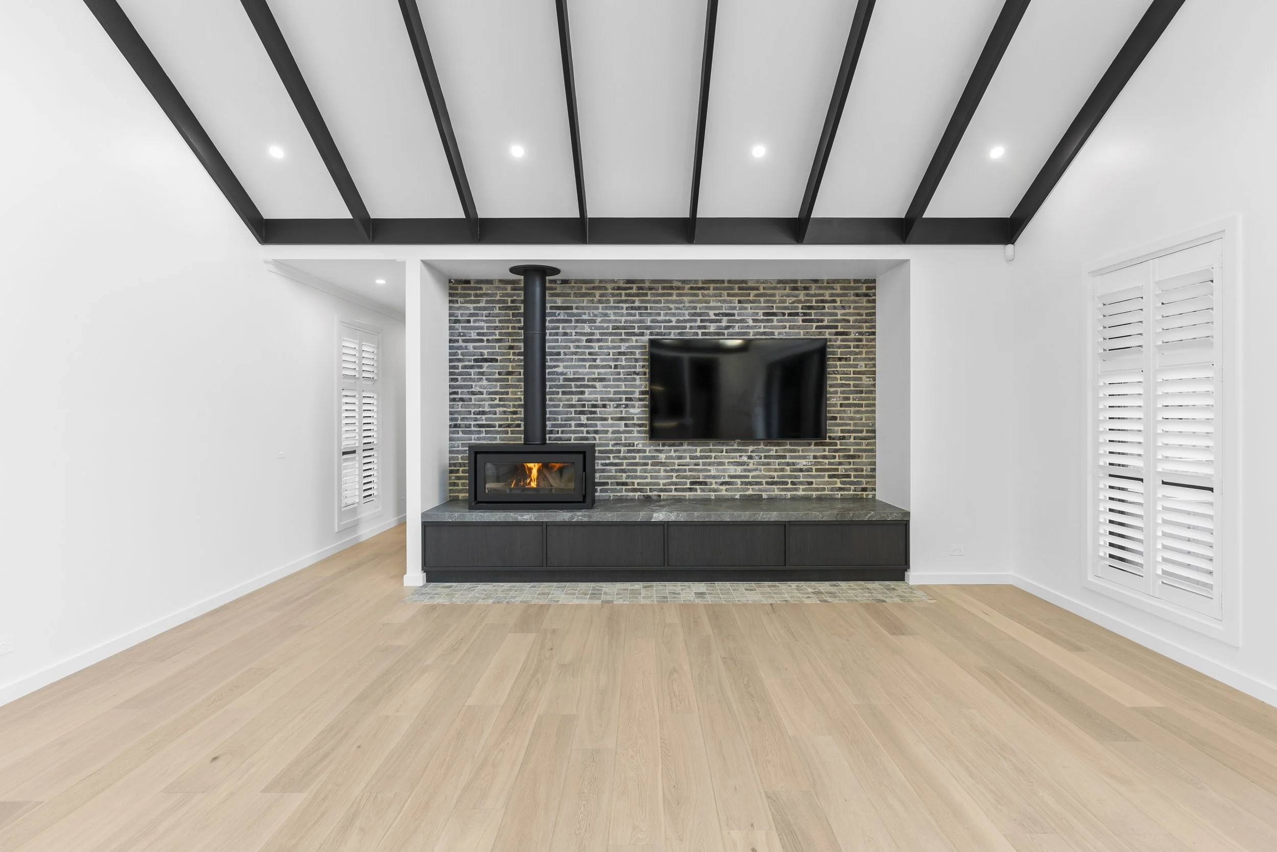 Modern living room with a fireplace, a mounted television, white walls, and light wood flooring.